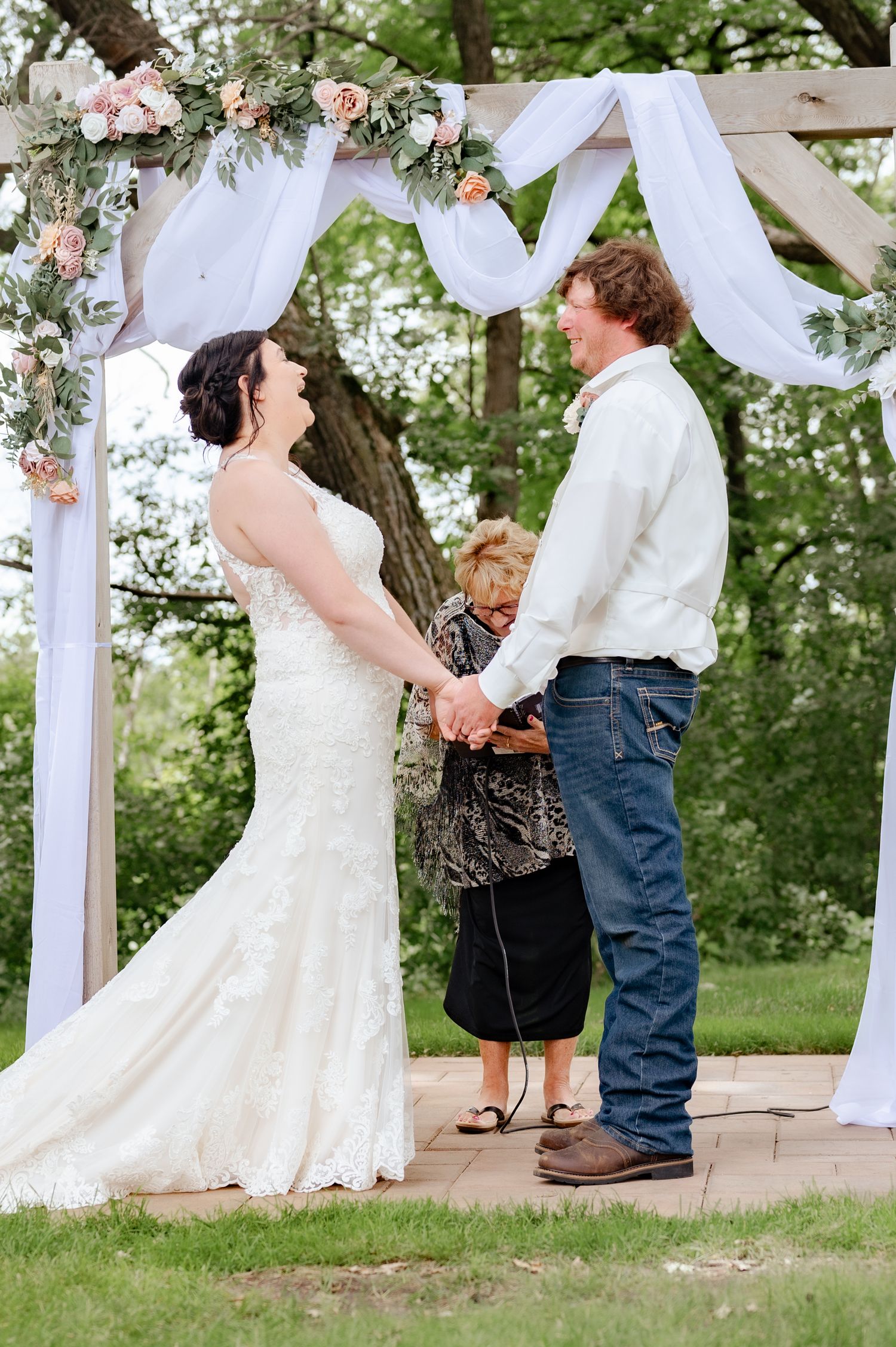Wedding ceremony under a white fabric arch decorated with pink roses and greenery.