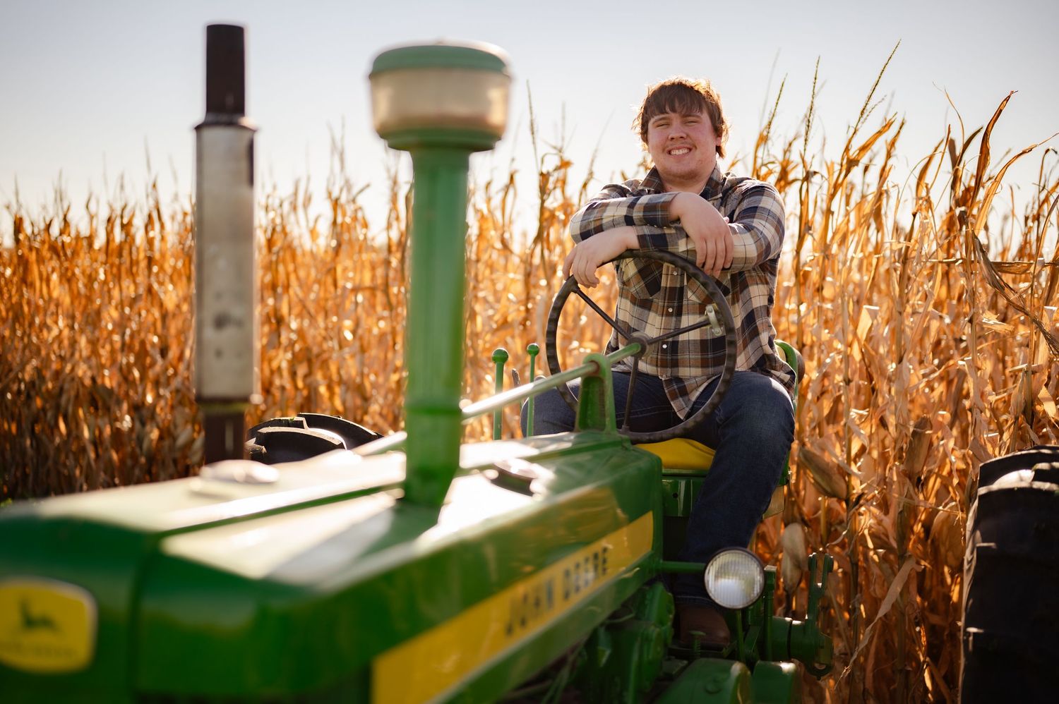 A farmer operates a John Deere combine harvester in a golden cornfield during autumn harvest season.