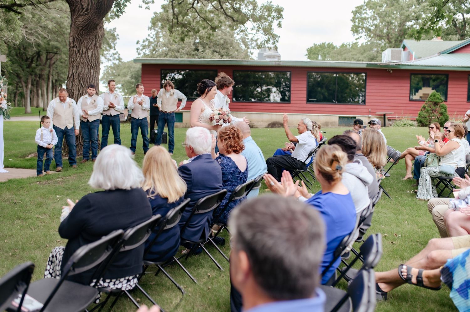 Wedding guests seated outdoors watching ceremony in front of pink building.