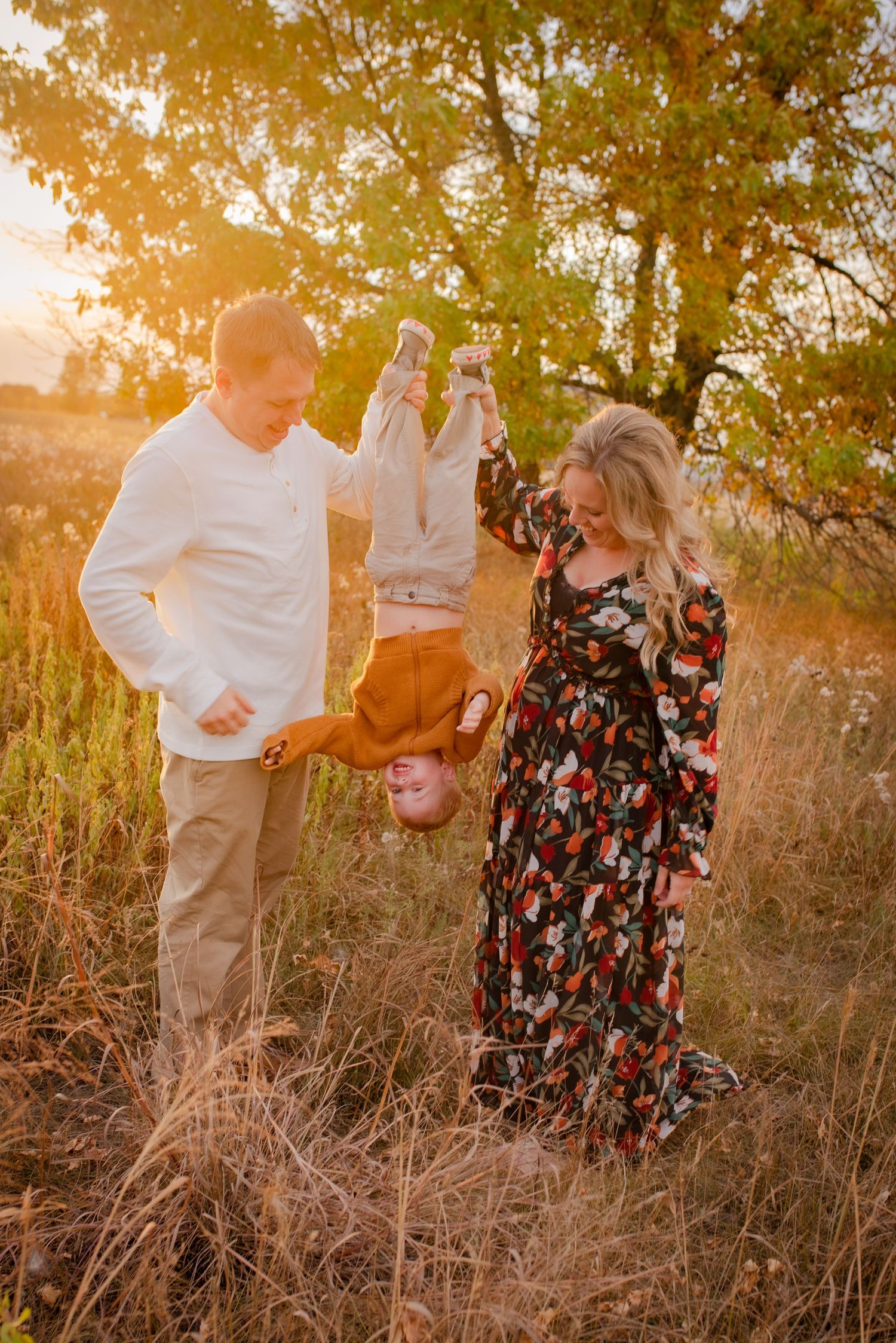 A family plays together against a golden sunset backdrop, swinging a laughing child upside down.