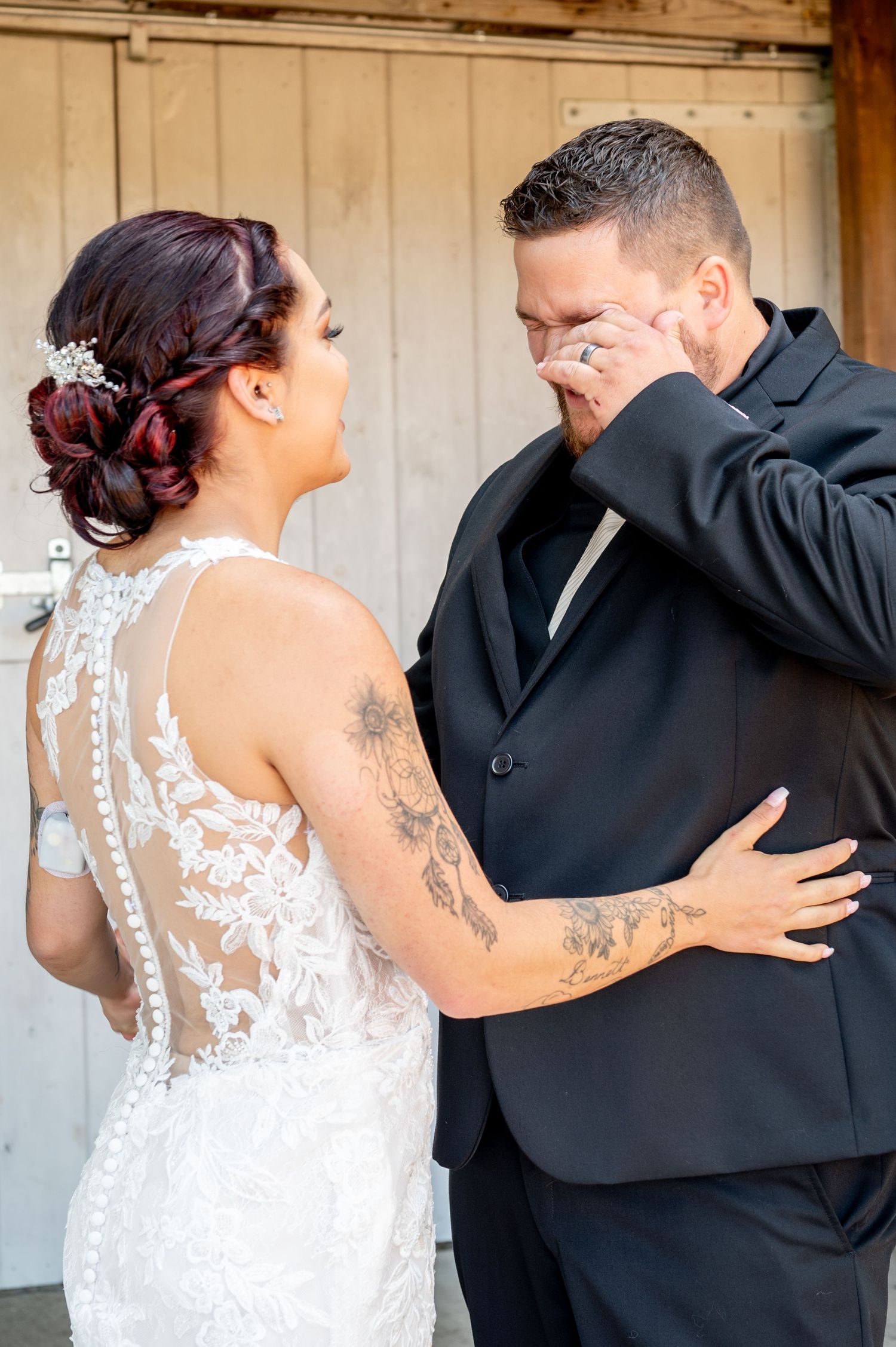 Bride in lace gown laughs as groom wipes tears during an emotional first look wedding moment.