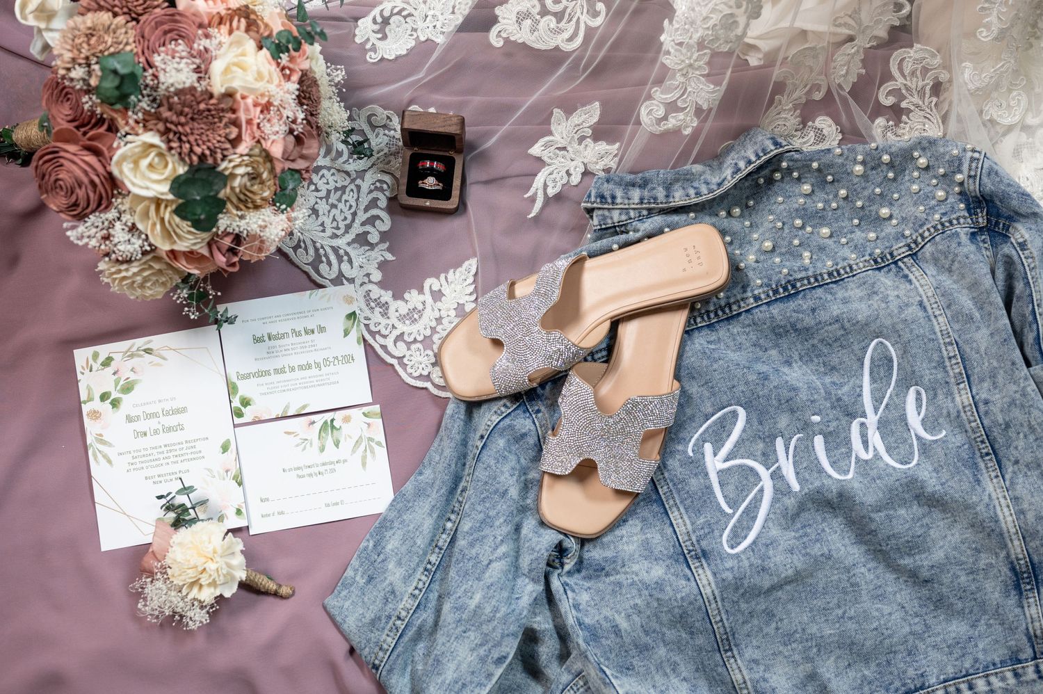 Wedding details including denim jacket with 'Bride' text, invitations, and floral arrangements on pink fabric.