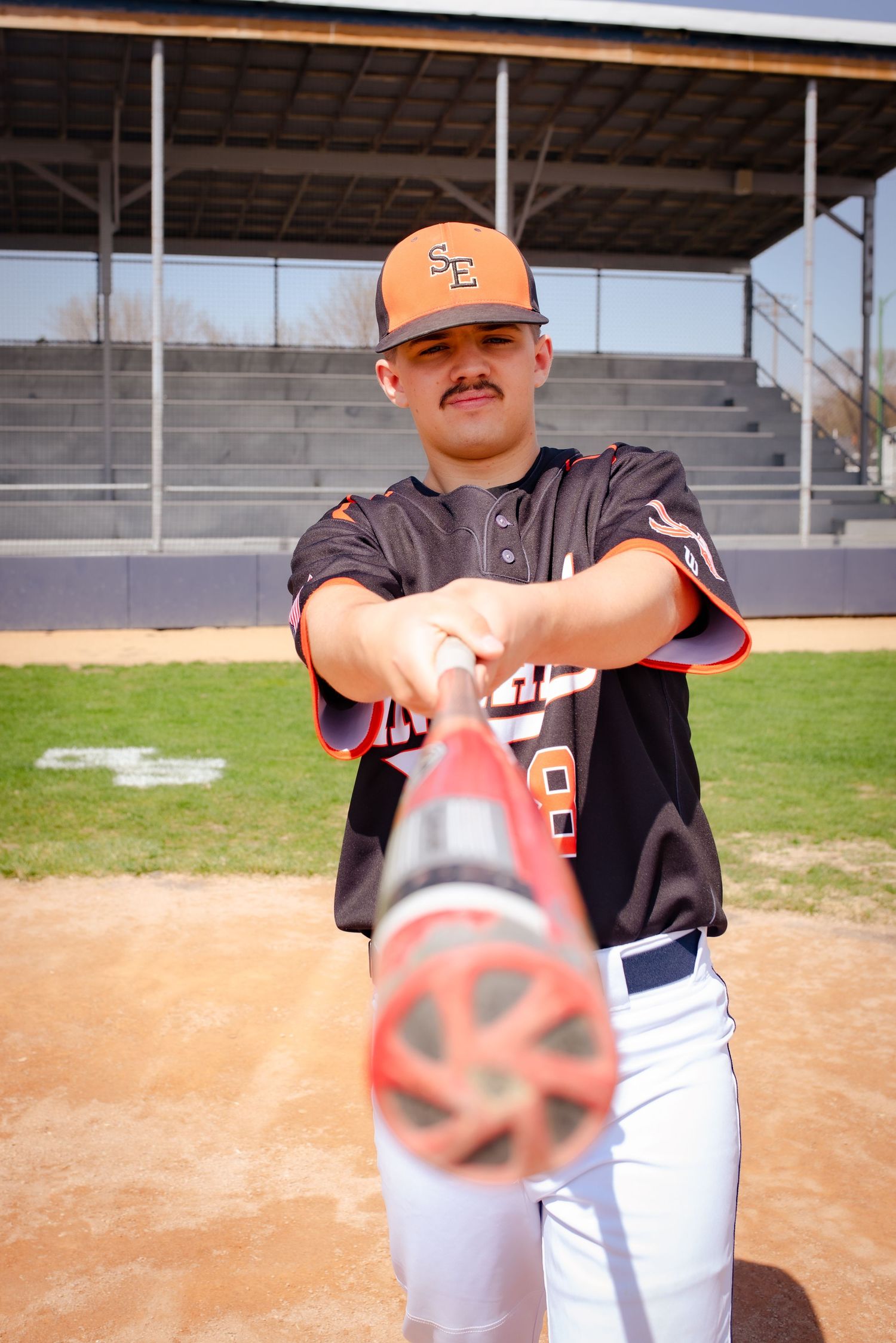 Baseball player in black uniform swings bat during practice with spinning ball effect.