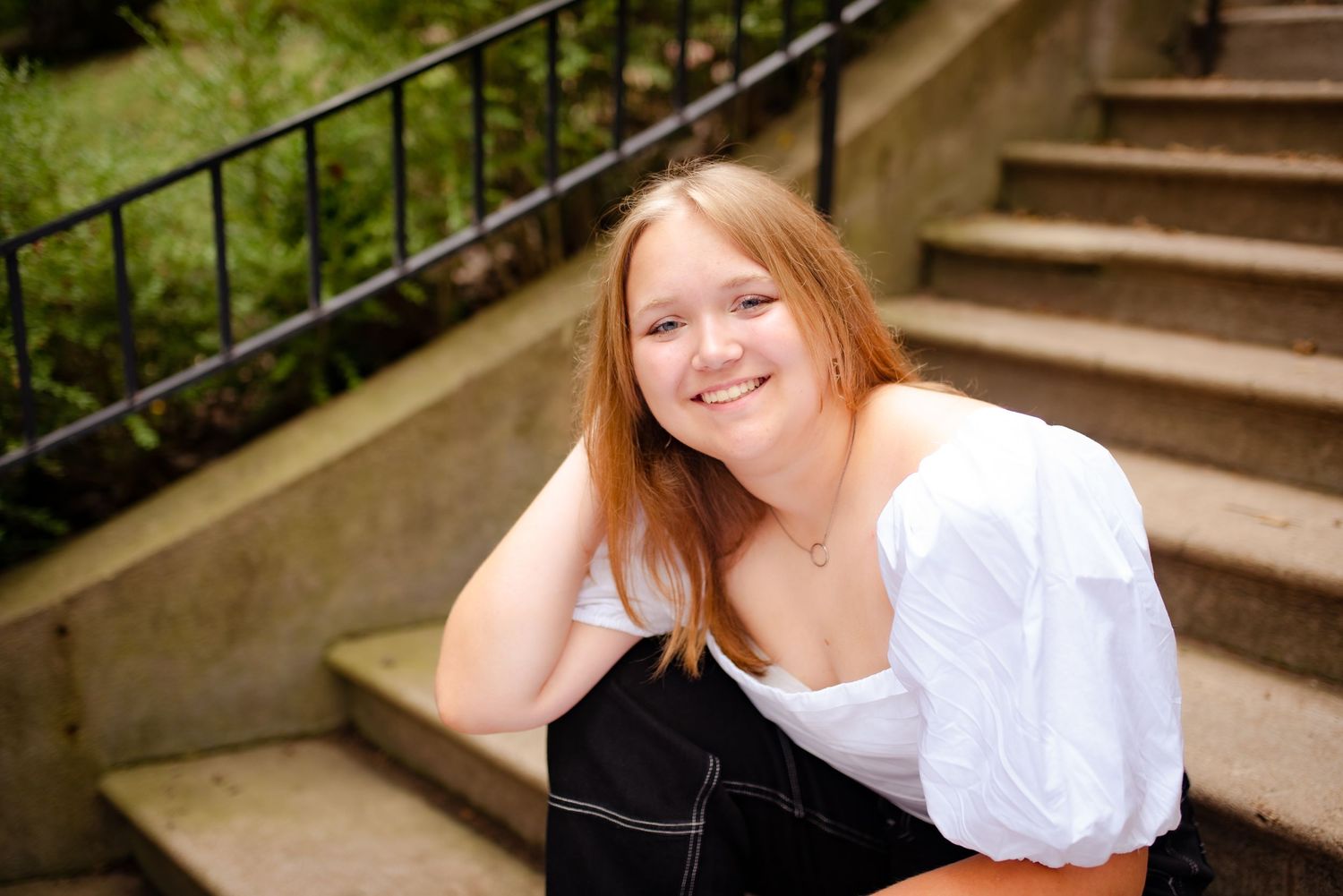 Portrait against concrete stairs with person in white blouse and dark pants.