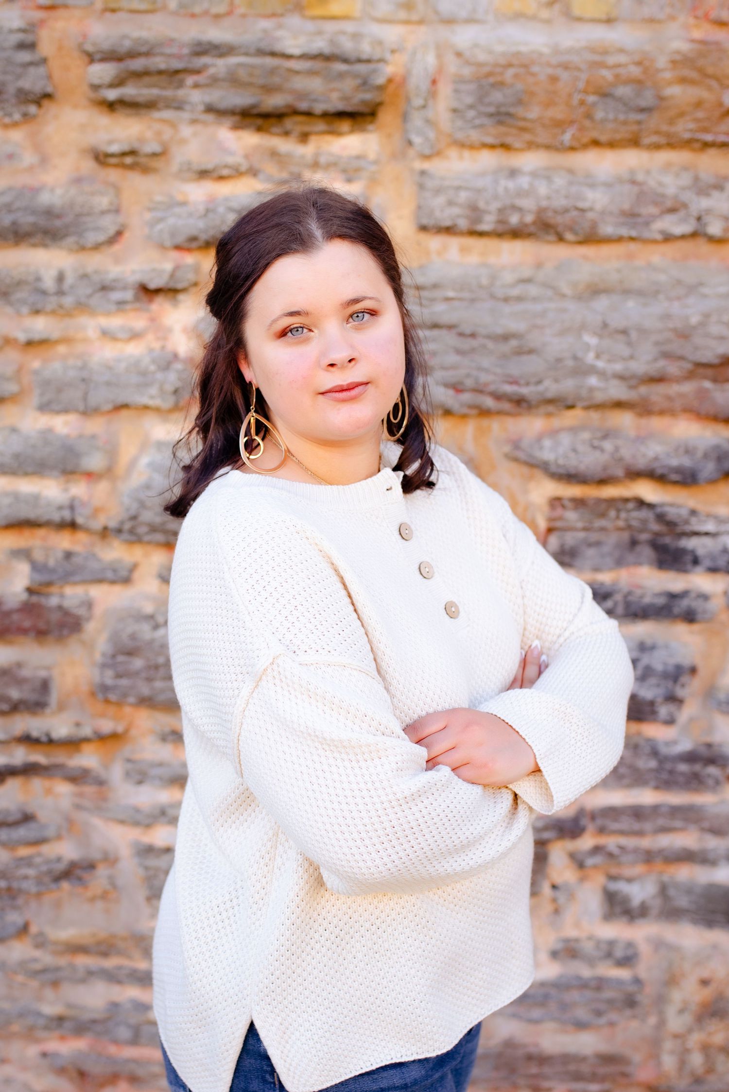 Person in cream knit sweater with buttons poses against textured stone wall.