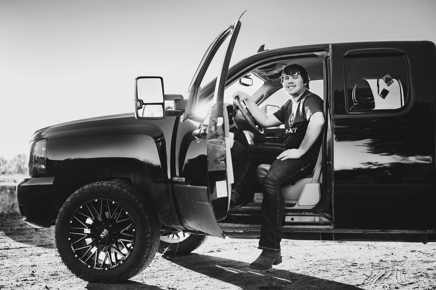A black and white photo of someone stepping out of a lifted black truck with large off-road tires.