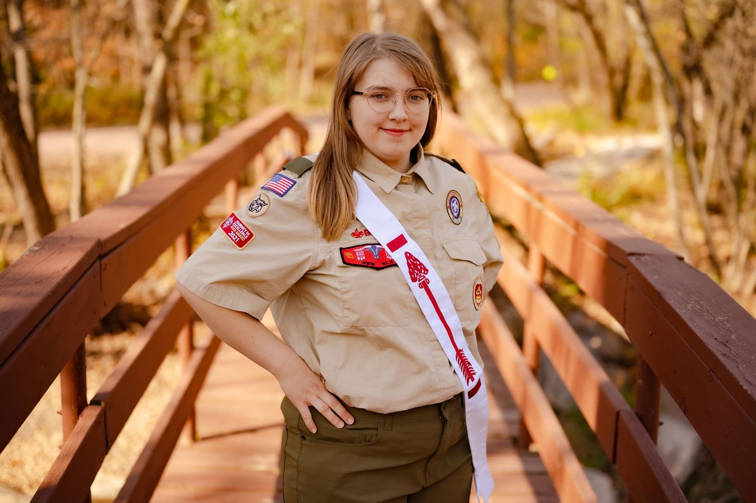 Person in scout uniform sits on wooden bridge during autumn season.