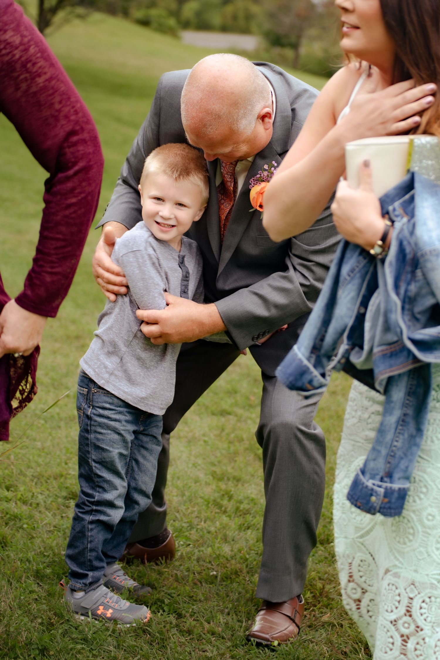 A young boy shares a tender moment with an older gentleman in formal attire at an outdoor gathering.