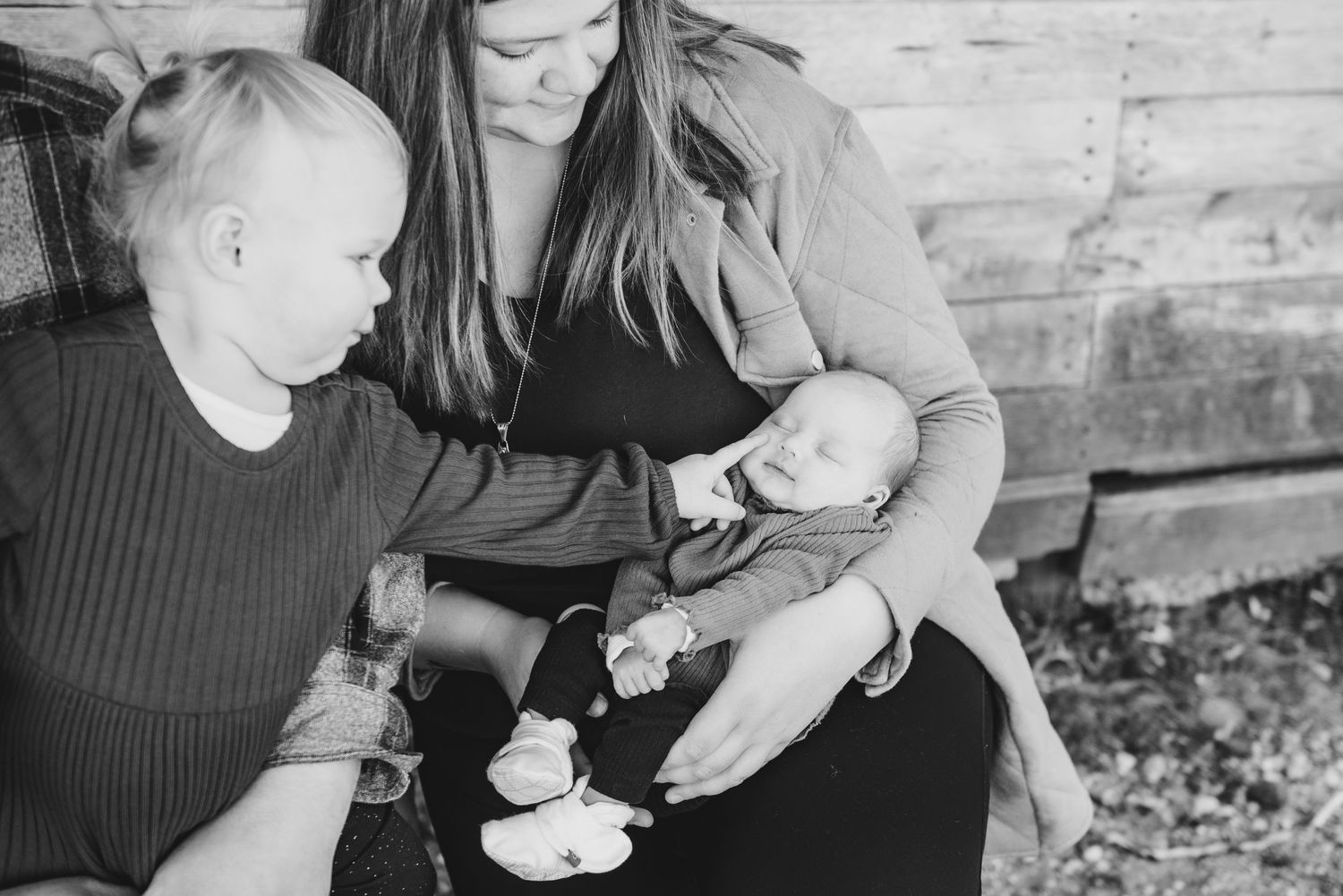 A tender family moment showing an infant being cradled while another child looks on in black and white.
