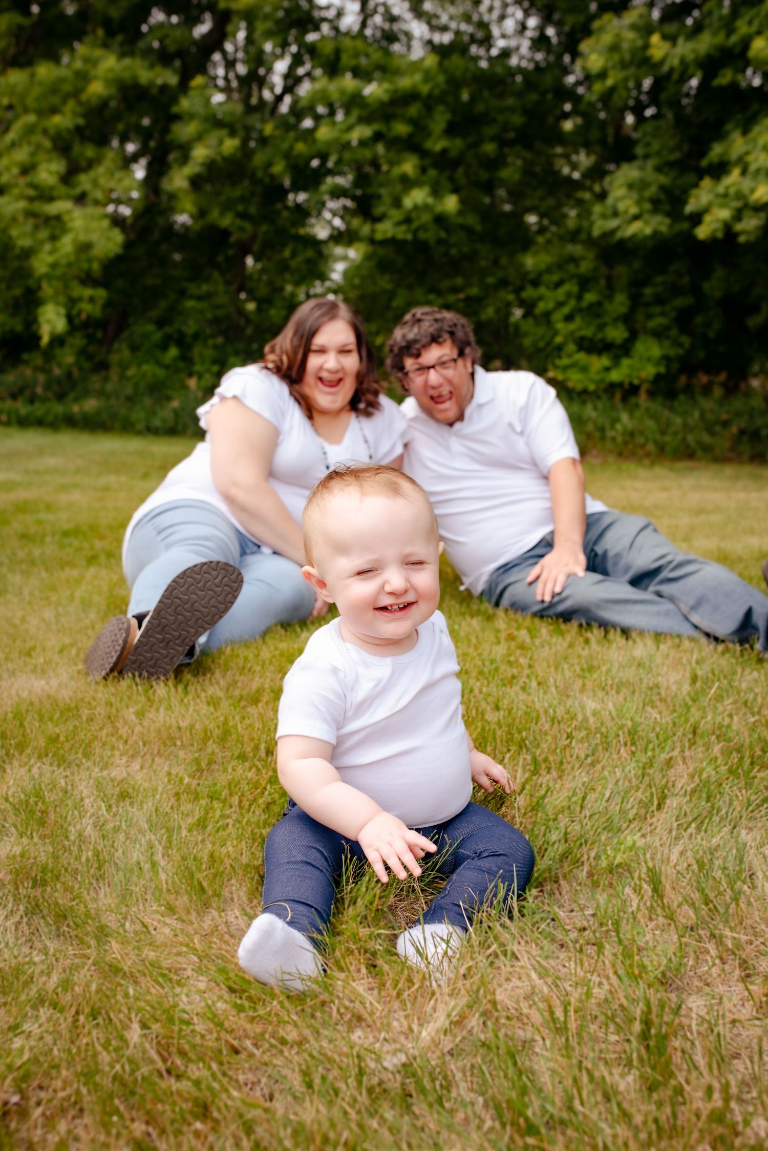 Candid family moment with laughing toddler in foreground and parents relaxing behind.