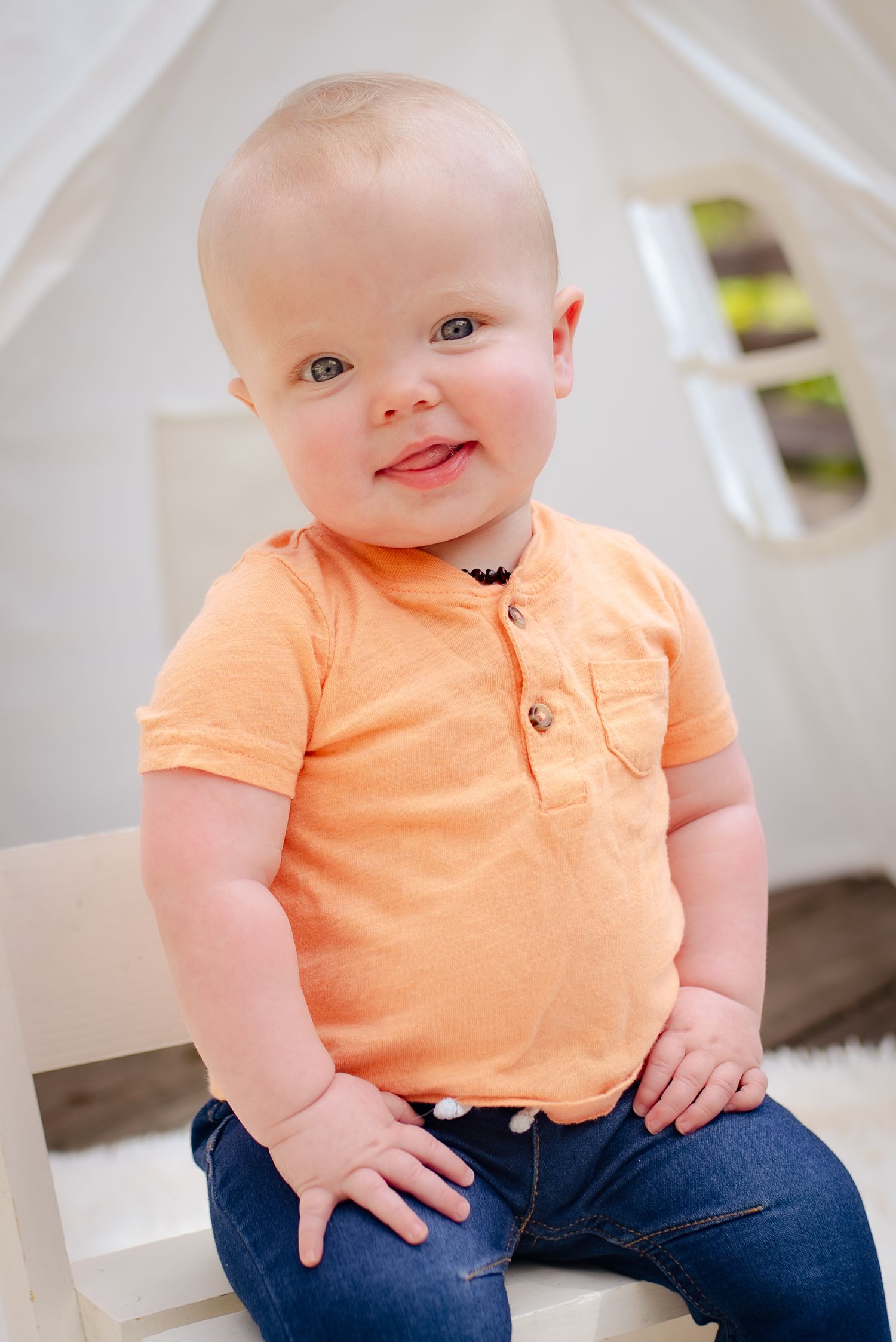 A toddler wearing a peach colored polo shirt and jeans smiles while sitting on stairs.