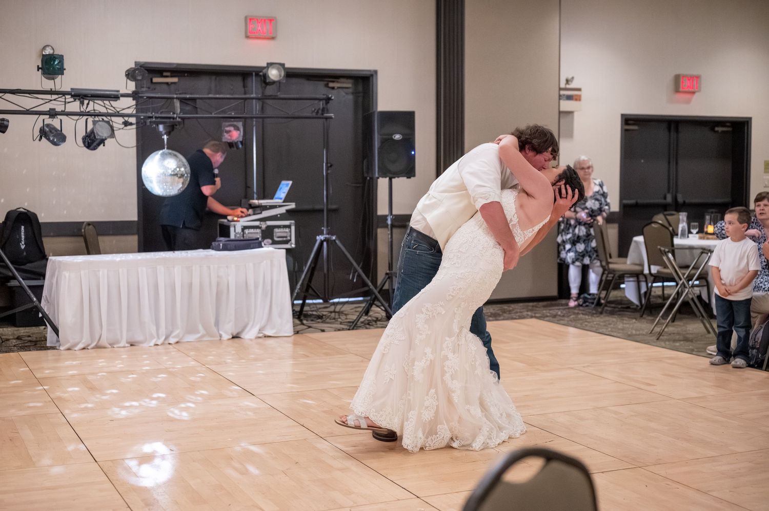 Newlyweds dance together on a reception hall dance floor with guests watching.