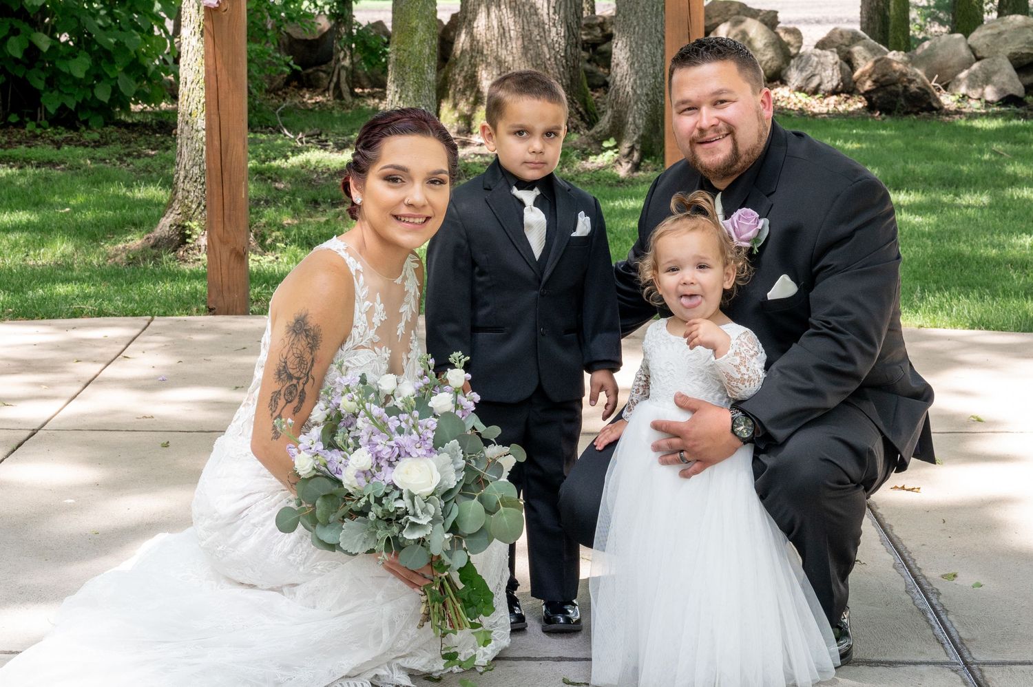 Wedding portrait of group seated together under pavilion with floral bouquet.