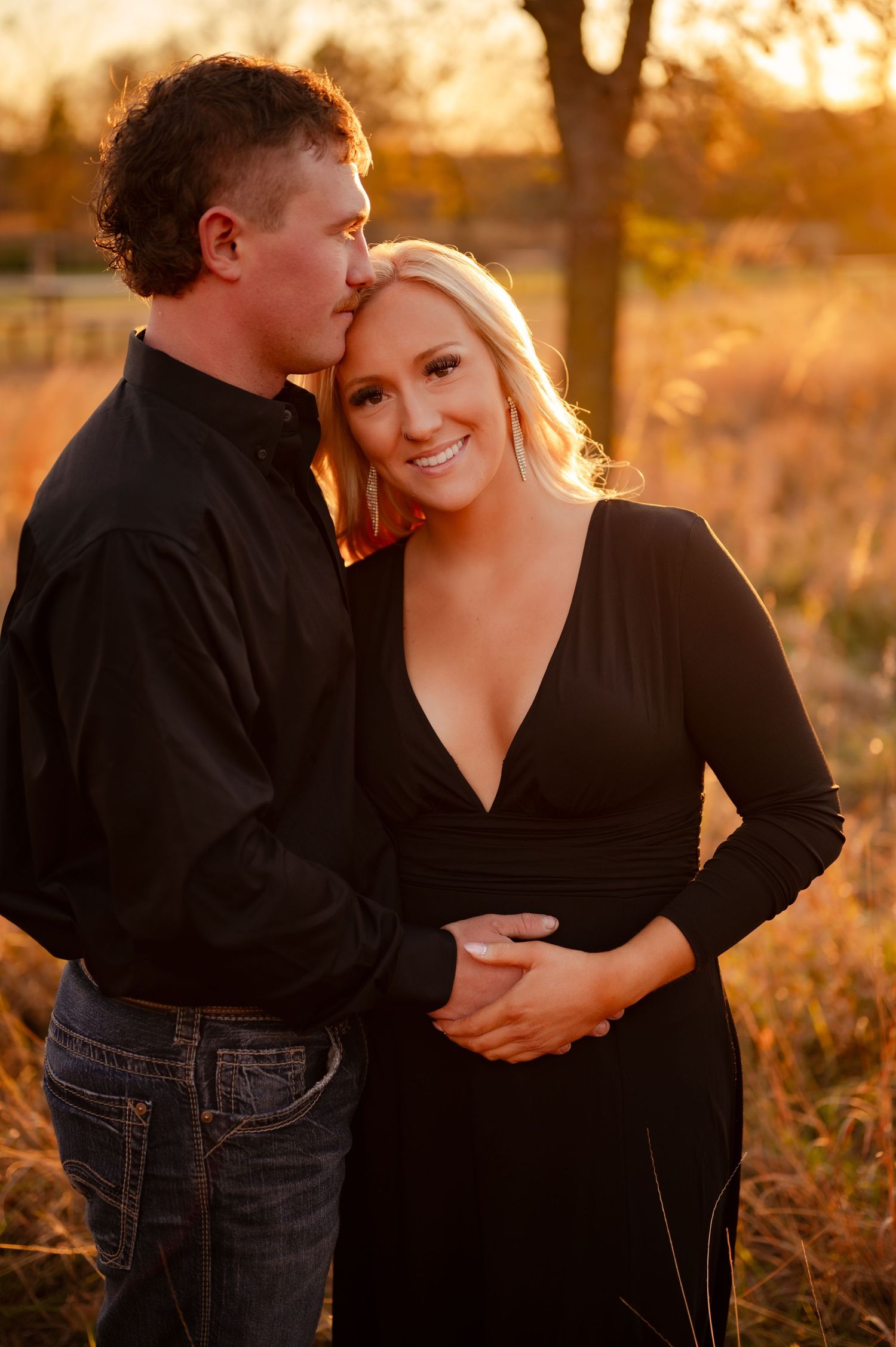 Romantic couple embracing in a field at sunset wearing black and denim casual outfits.