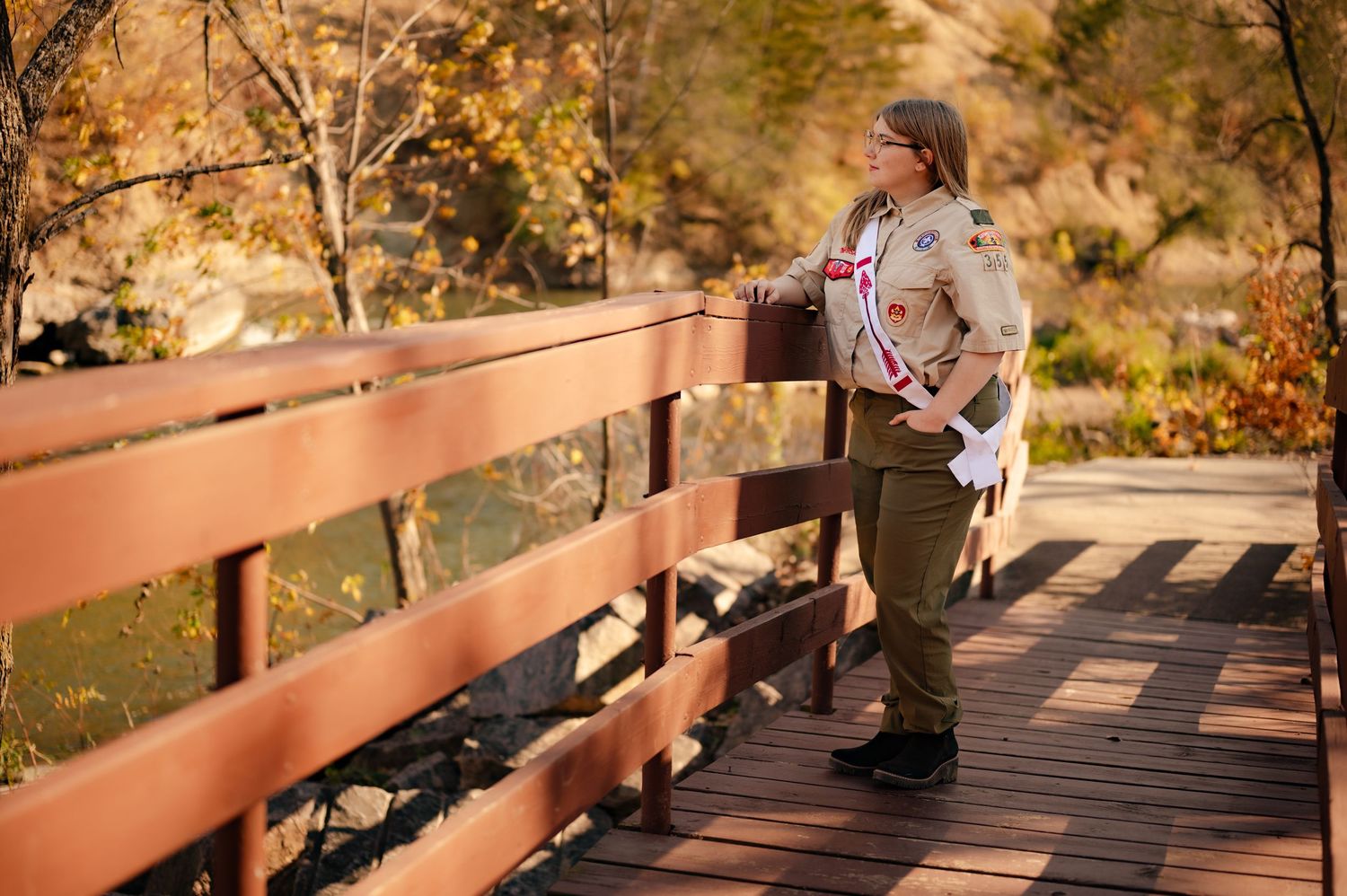 Wooden footbridge extends through autumn foliage with golden sunlight filtering through trees.