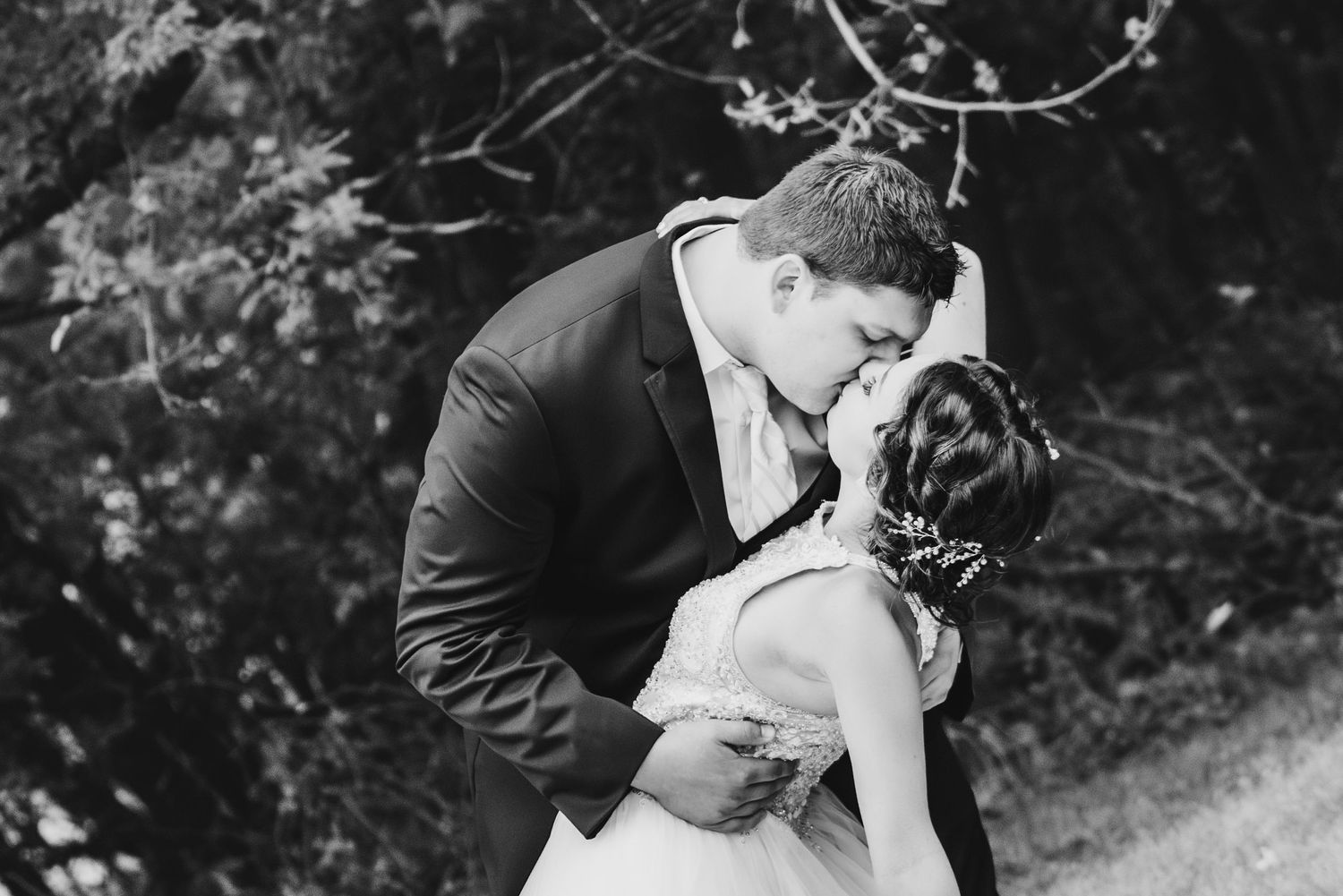 Romantic dip kiss between newlyweds surrounded by natural outdoor scenery.