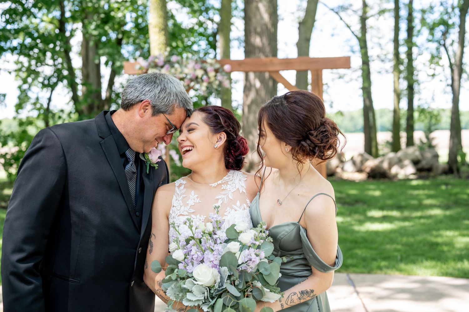 Wedding party sharing a joyful moment outdoors with white flowers and greenery in the background.