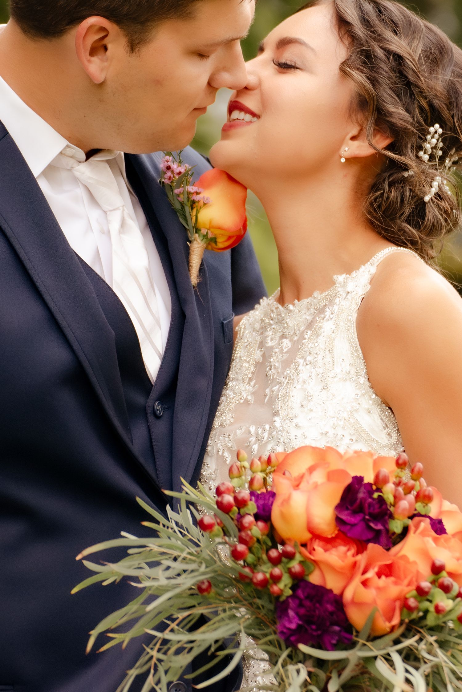Close-up wedding portrait with vibrant orange and purple bouquet as couple shares intimate moment.