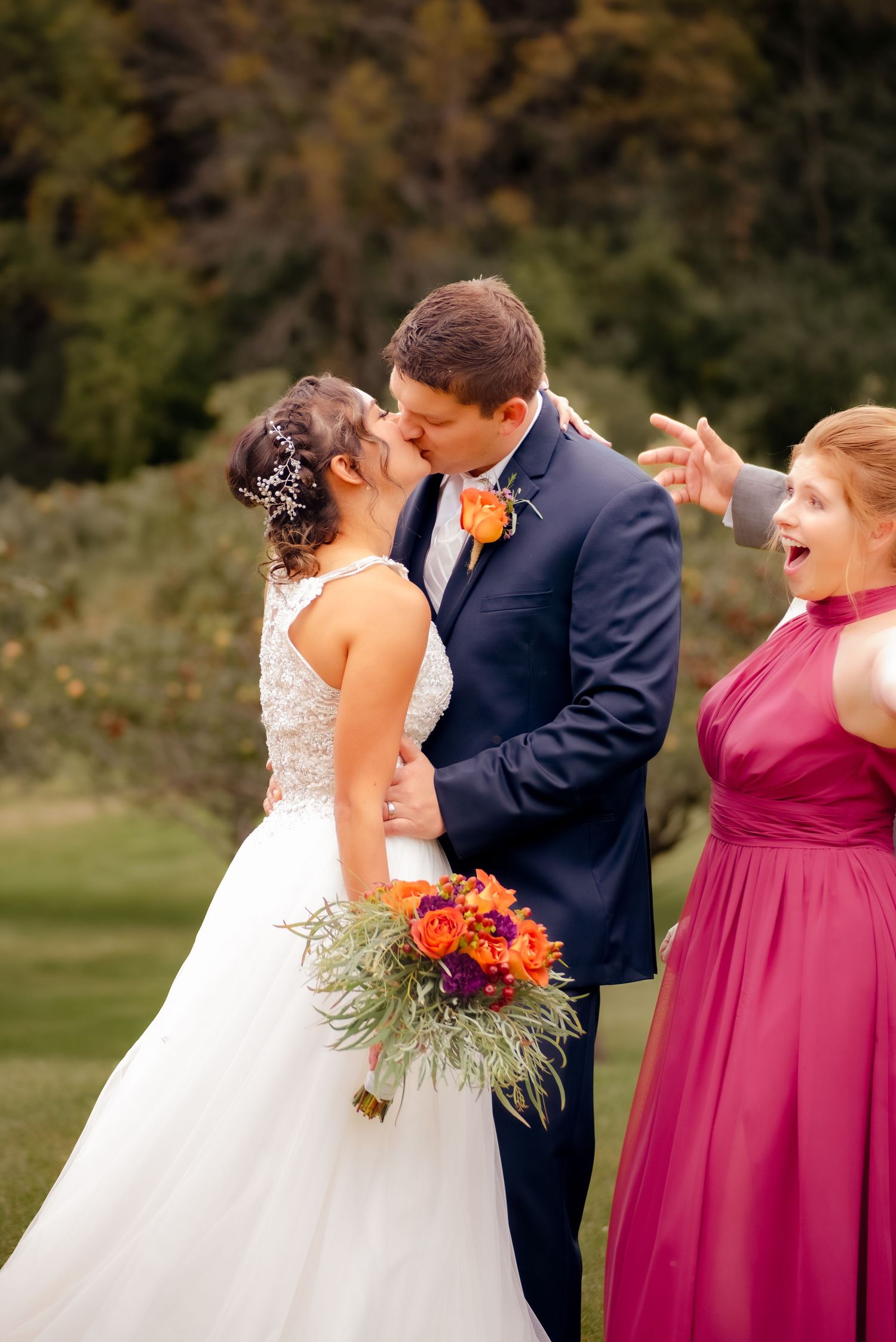 A romantic wedding moment captured outdoors with a bridesmaid in burgundy celebrating nearby.