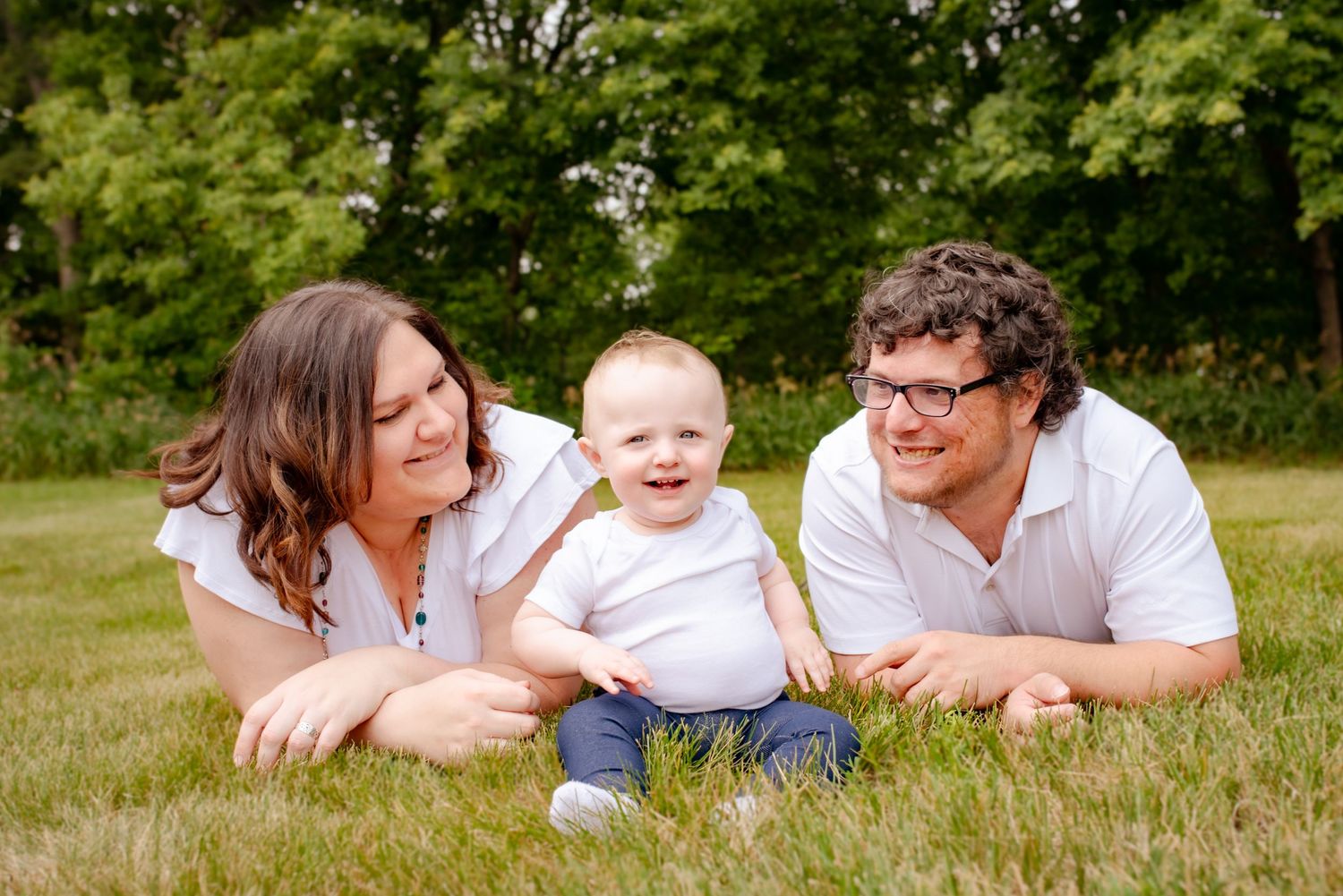 Family laying in grass together during summer photo session with leafy background.