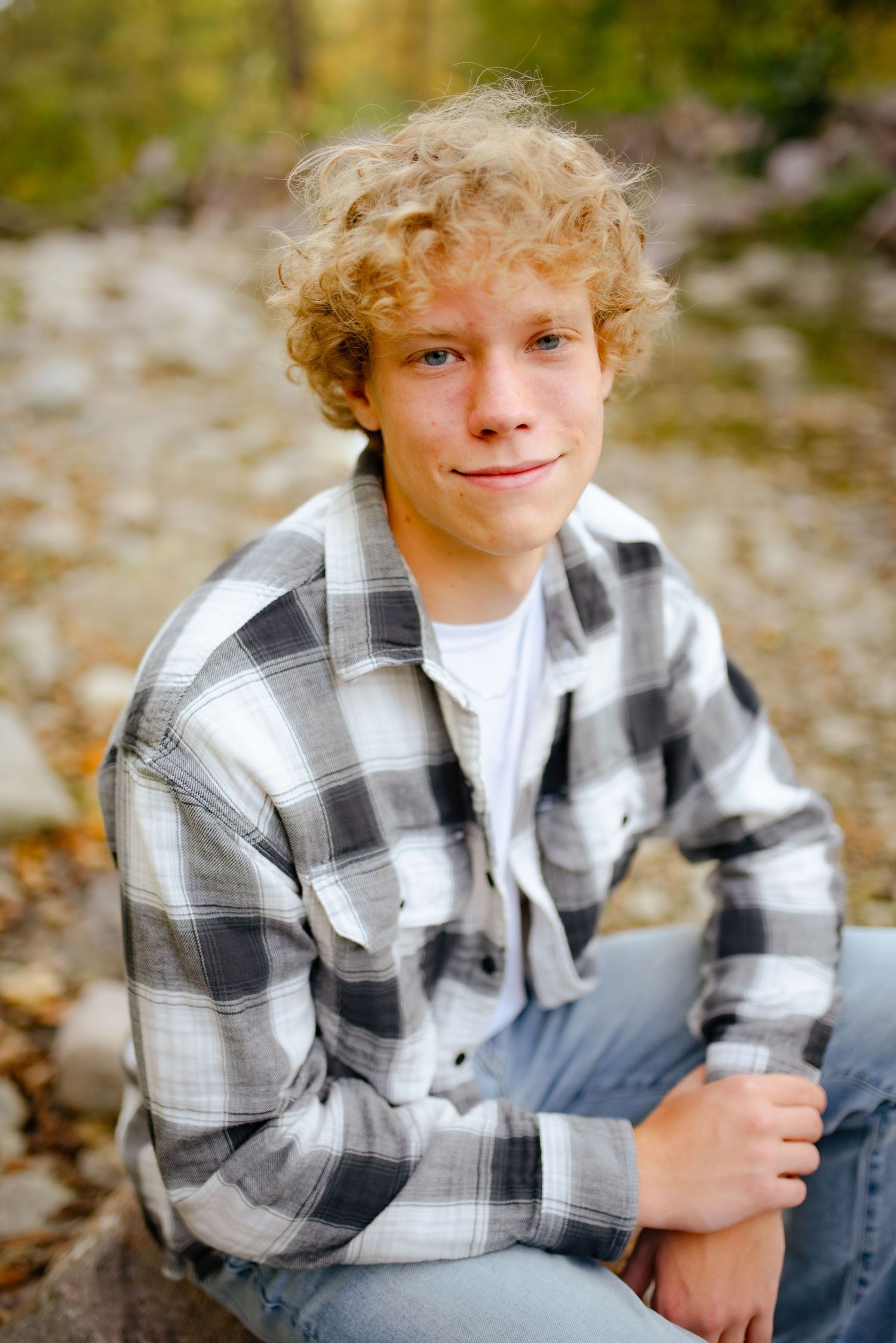 A casual portrait of someone sitting on rocks wearing a black and white plaid flannel shirt.
