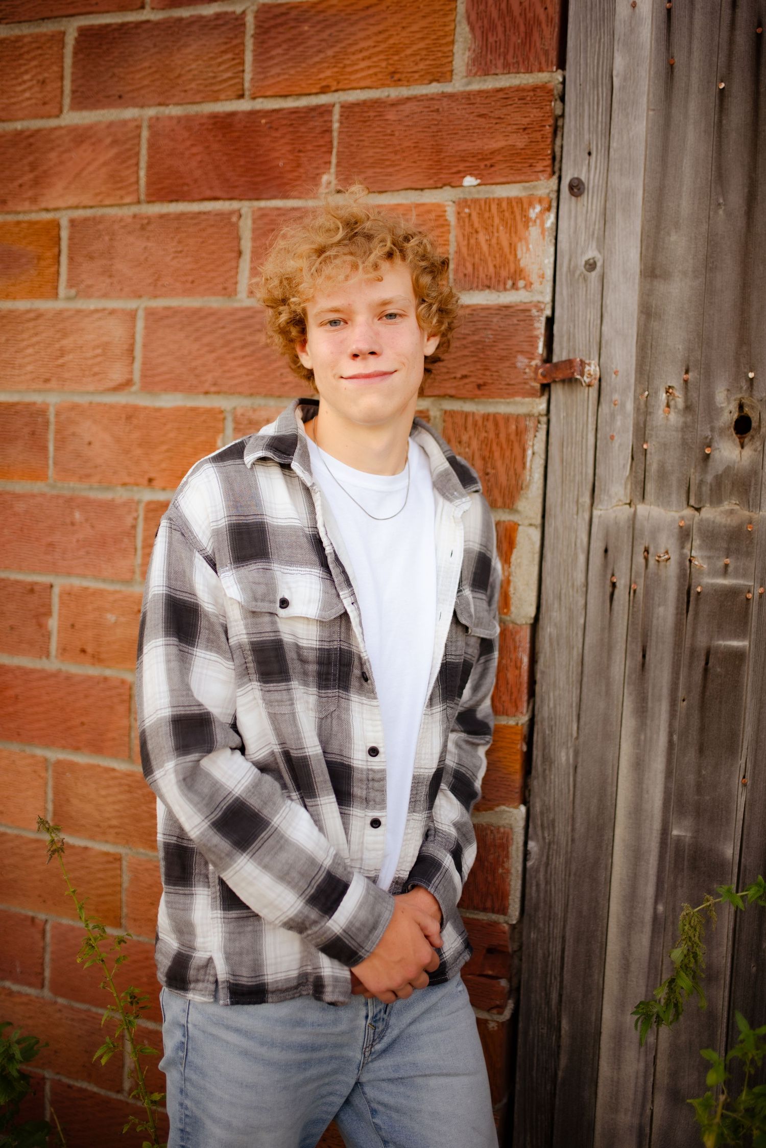 Casual portrait against red brick and wooden door wearing black and white plaid flannel shirt.