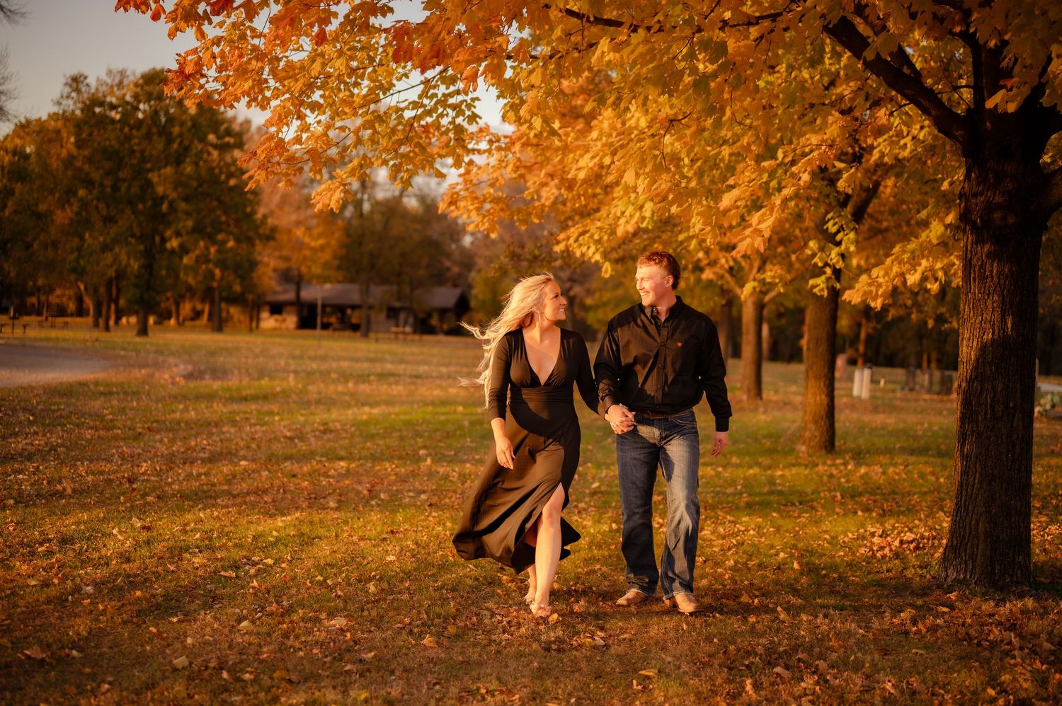 Two figures walk together through fallen autumn leaves at sunset.