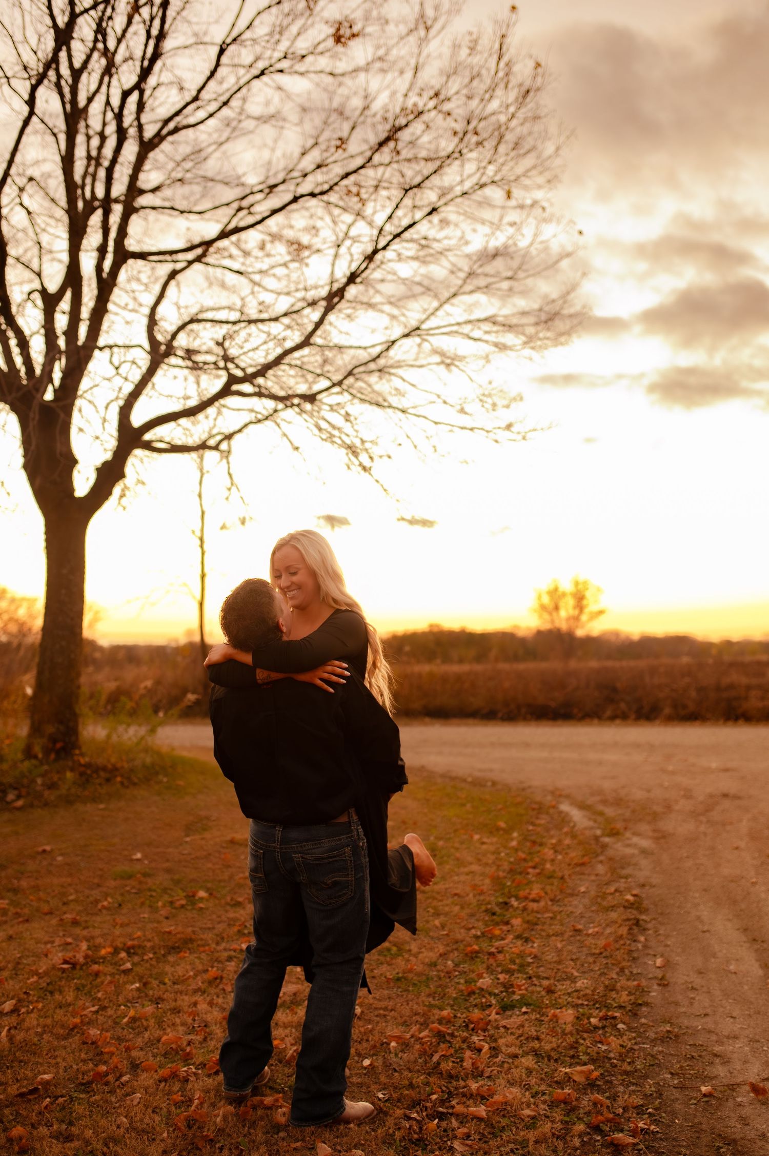 Intimate moment captured between two people on leaf-covered path at dusk.