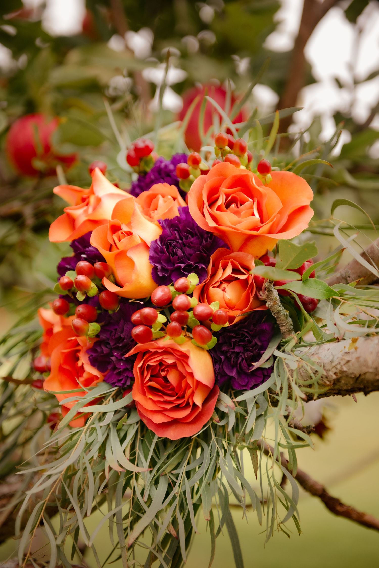 Vibrant wedding bouquet featuring coral roses and deep purple flowers with wispy greenery.