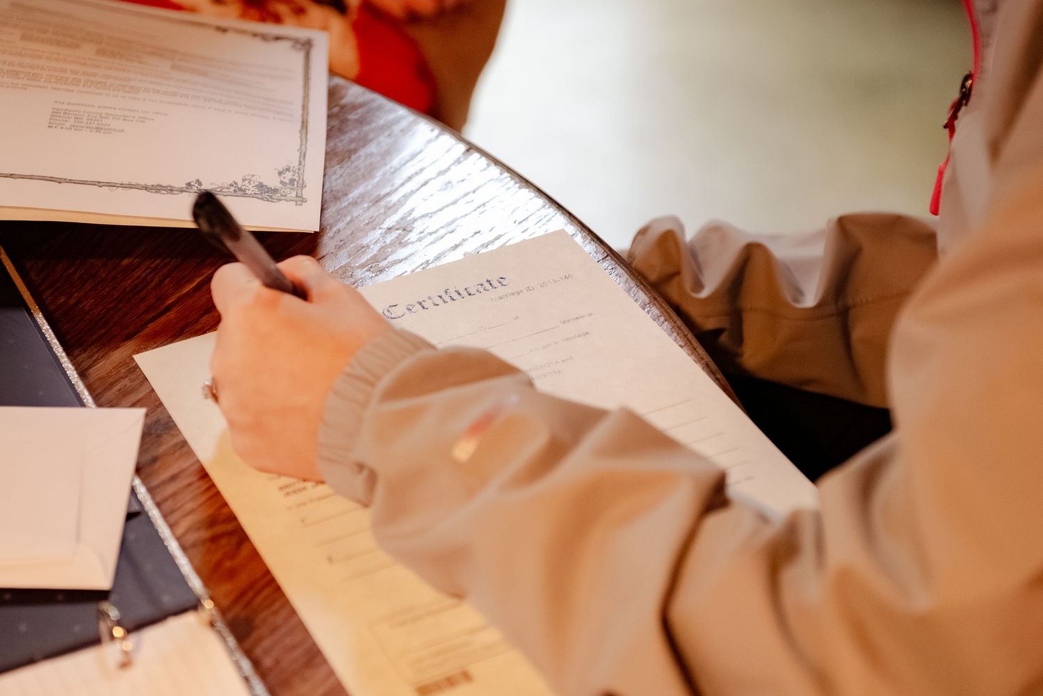 Wedding paperwork and documents being filled out on a wooden surface.