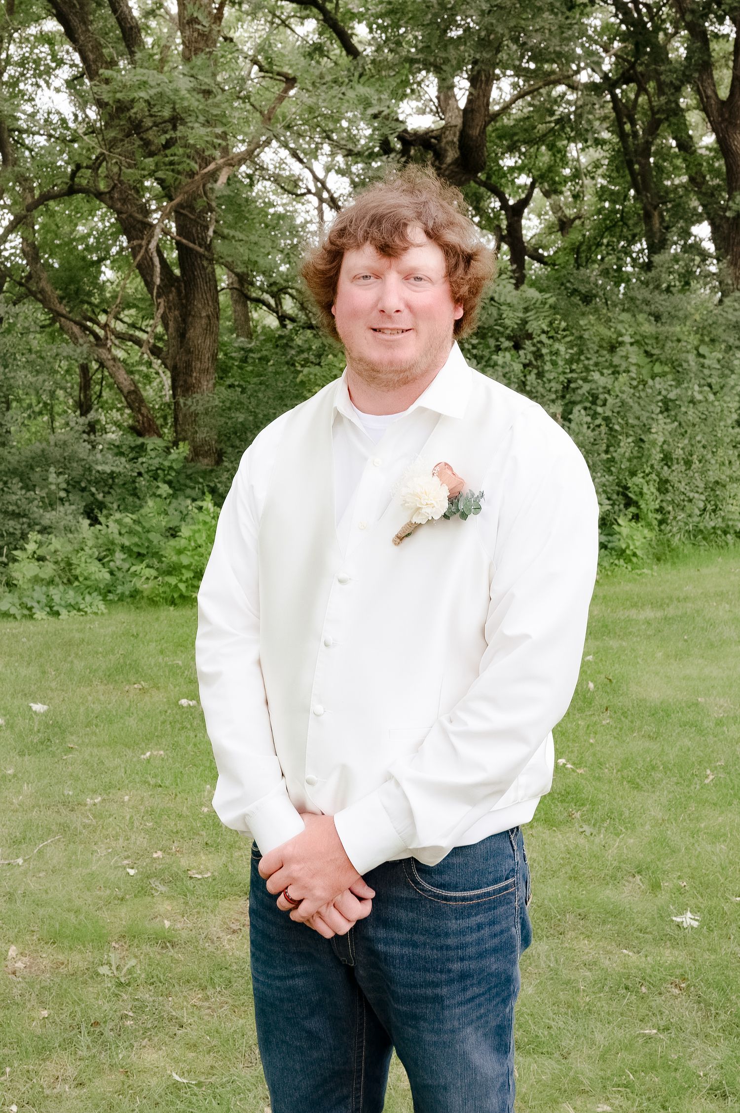 Person in white dress shirt with boutonniere smiling outdoors.