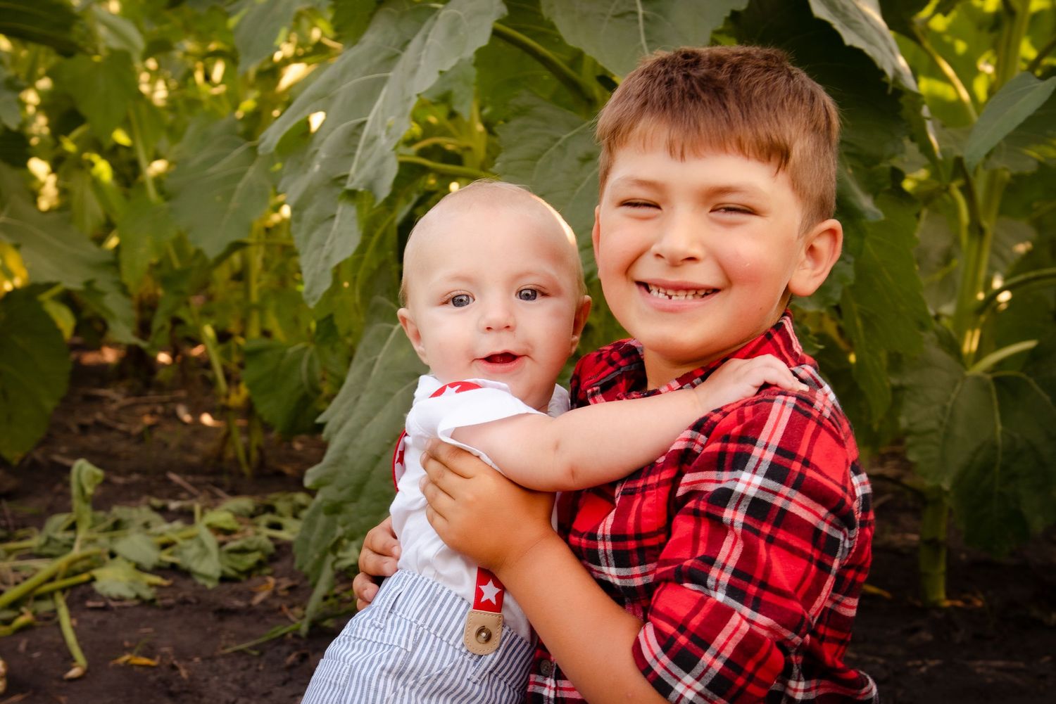 Heartwarming outdoor portrait of two children sharing joyful smiles among green foliage.