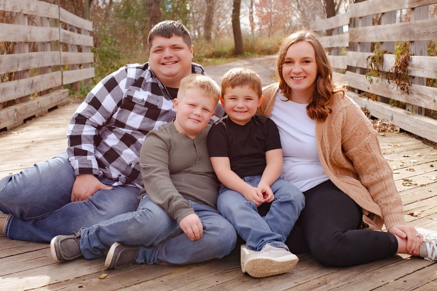 Family sitting together on rustic wooden bridge for casual outdoor portrait.