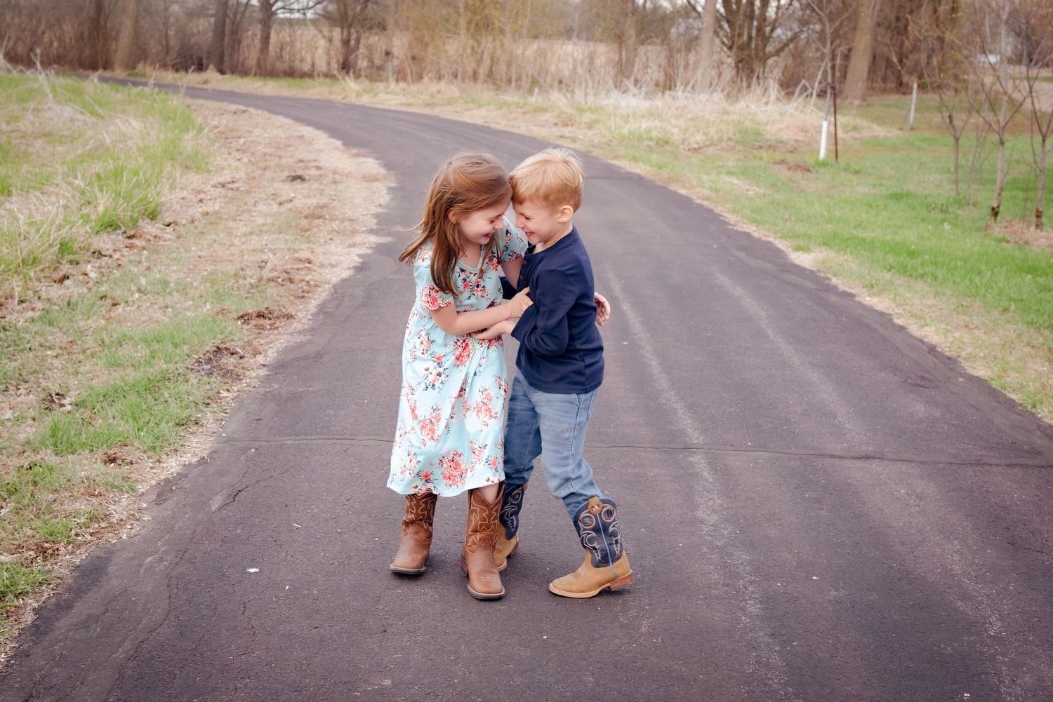 Two kids sharing a sweet moment together on a paved path surrounded by grass.