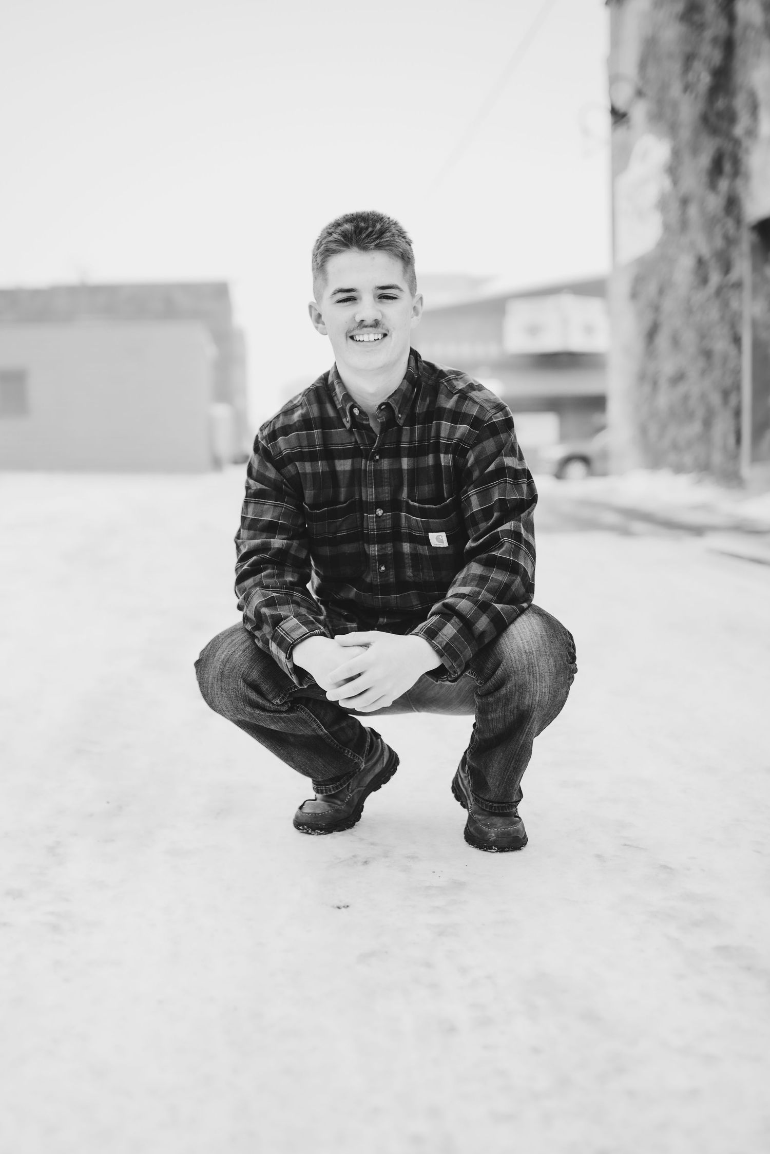Black and white outdoor portrait crouching in snow wearing plaid flannel.