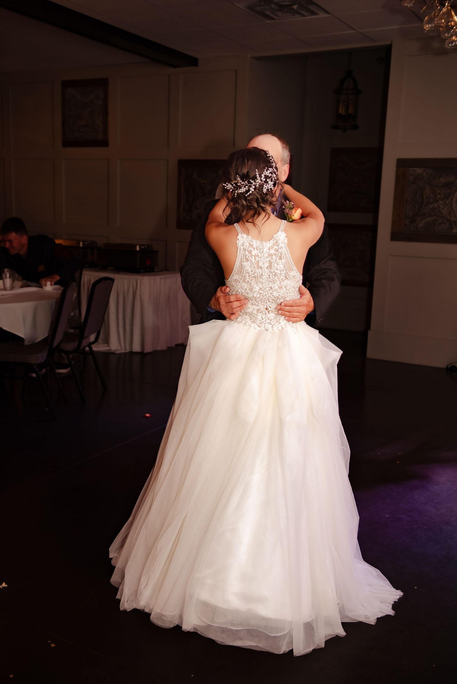 A bride in a flowing white gown dances gracefully in a reception hall with purple ambient lighting.