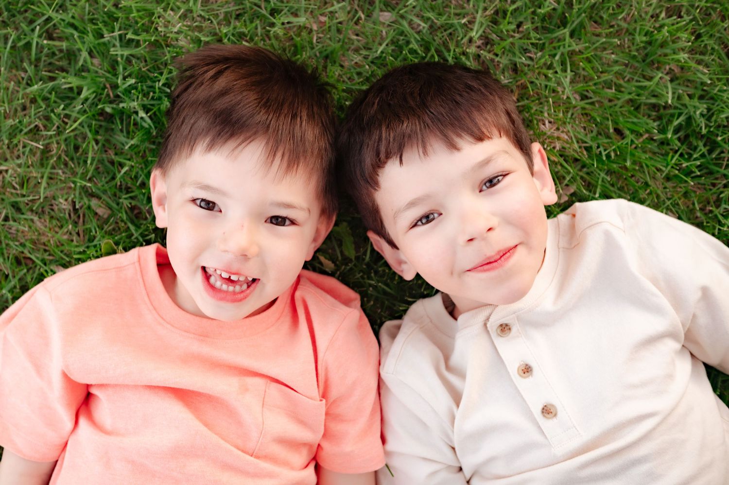 Two young children lying on grass together sharing joyful smiles.
