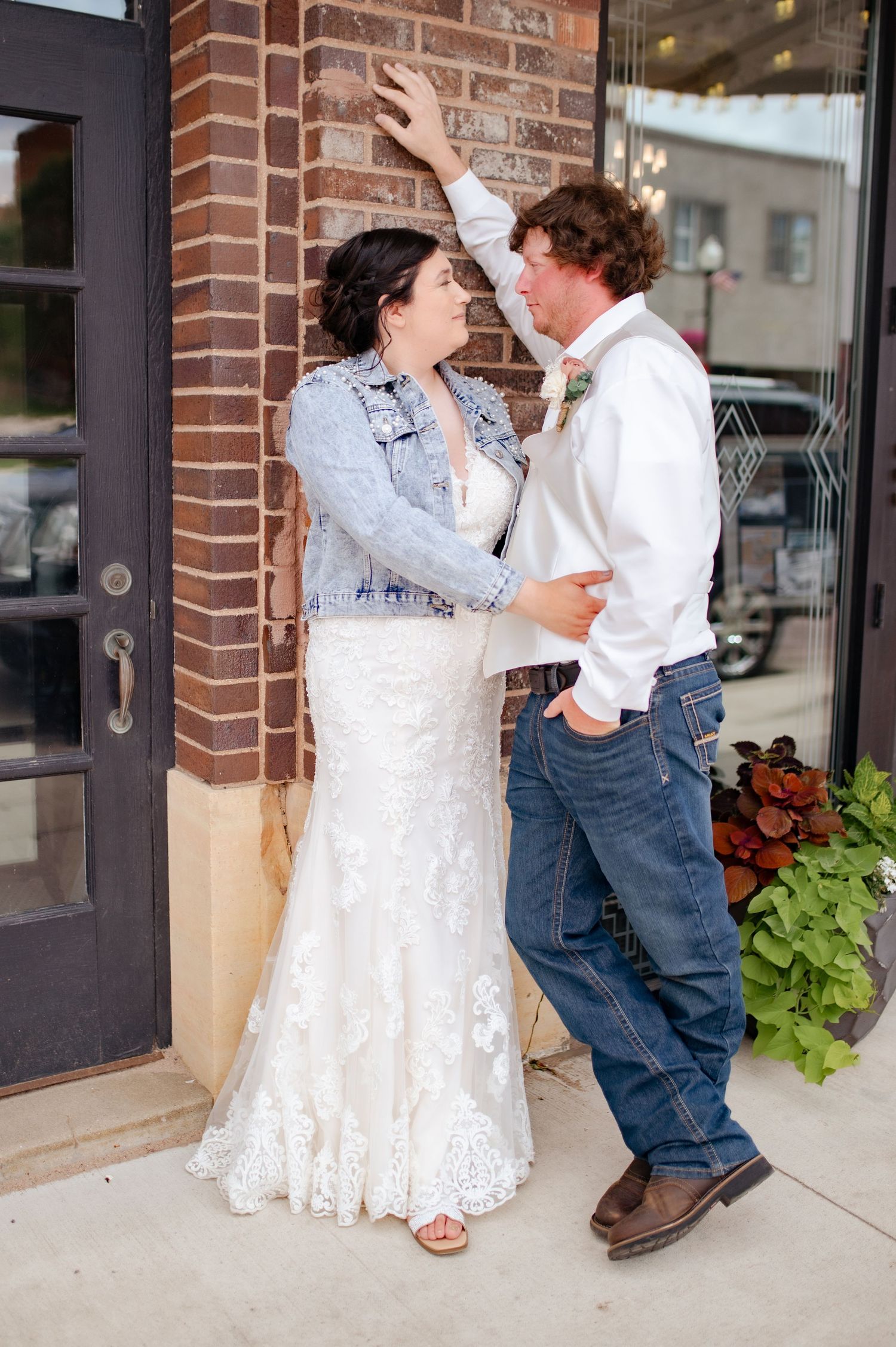 Casual wedding couple sharing a romantic moment against brick wall exterior with greenery.