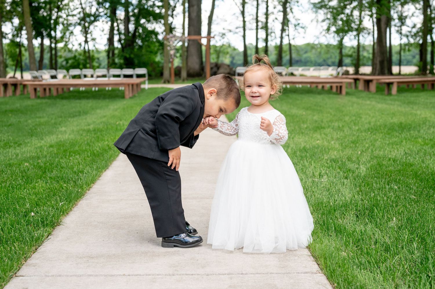 Sweet moment between ring bearer and flower girl on concrete path at outdoor wedding.