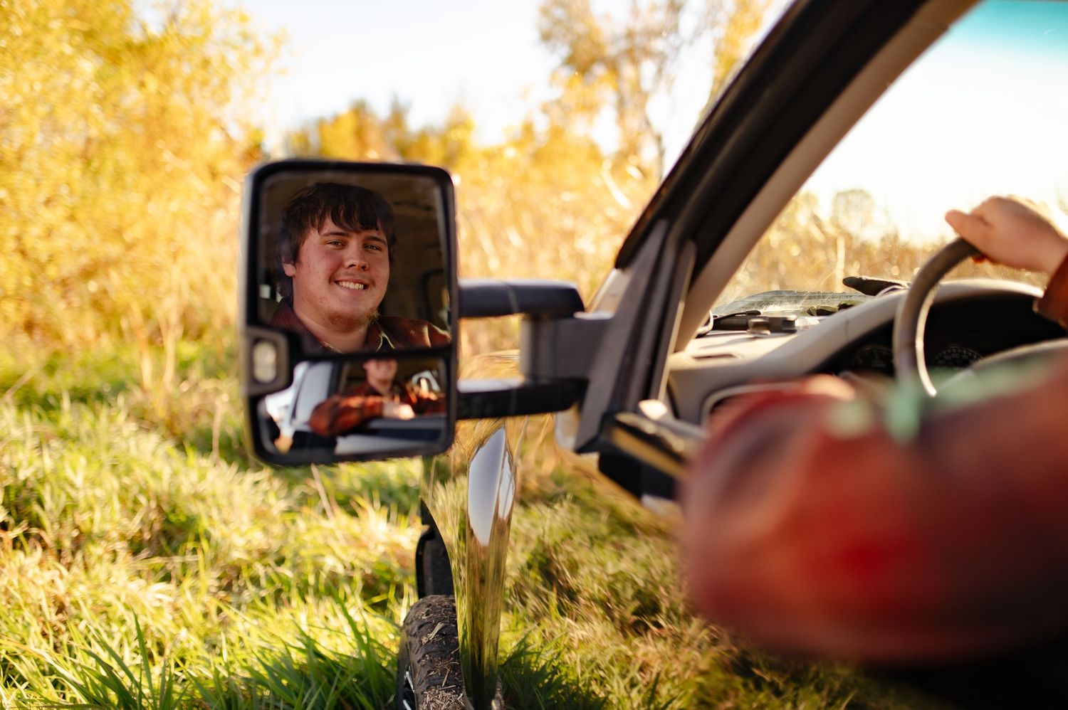 Interior view through car windshield and rearview mirror during sunset with golden lighting.