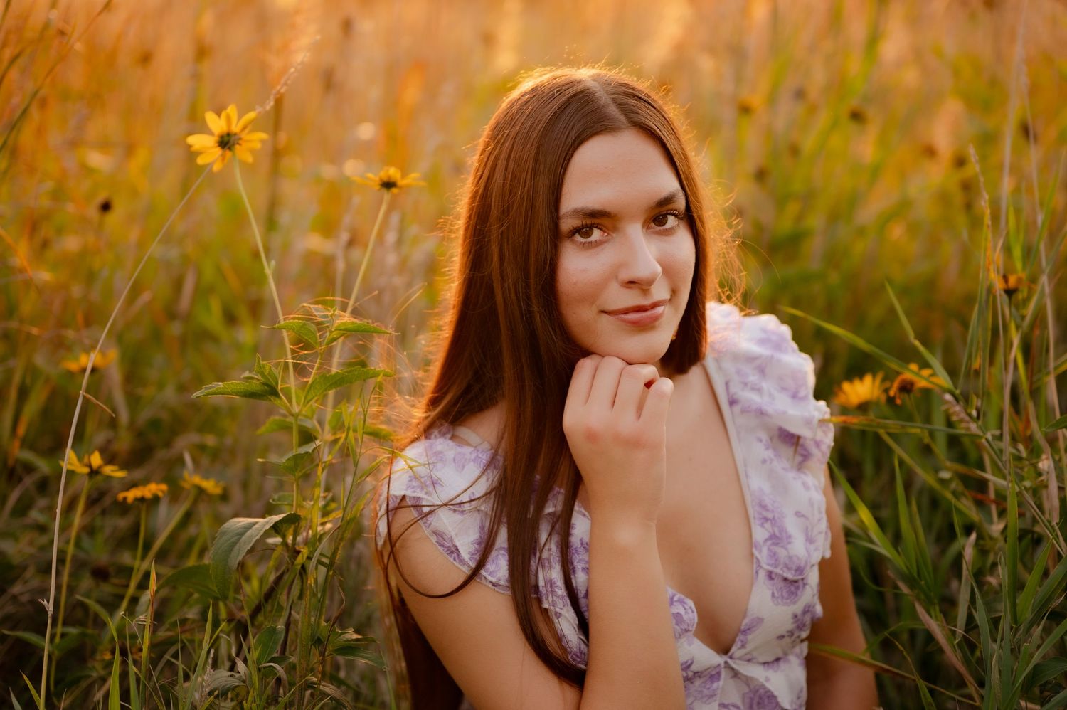A person in a white dress poses in a golden field during sunset with sunflowers in the background.