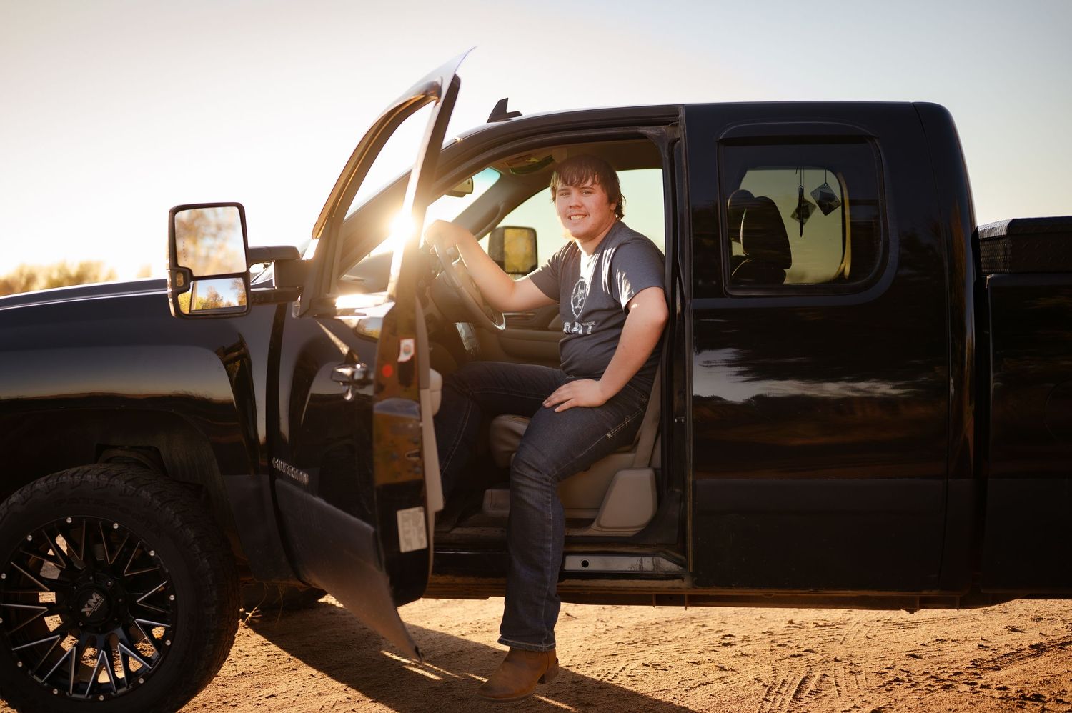 A black pickup truck parked in the desert during golden hour with sunlight streaming through the open door.