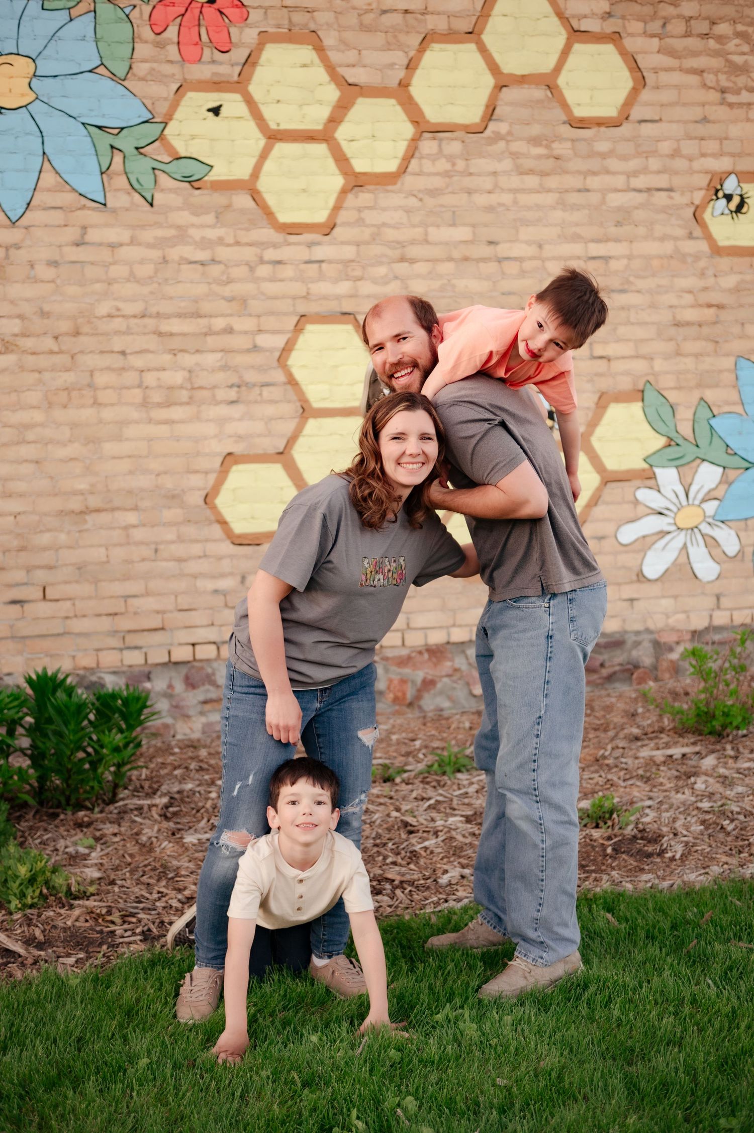 Family poses playfully in front of a brick wall with painted honeycomb and floral decorations.