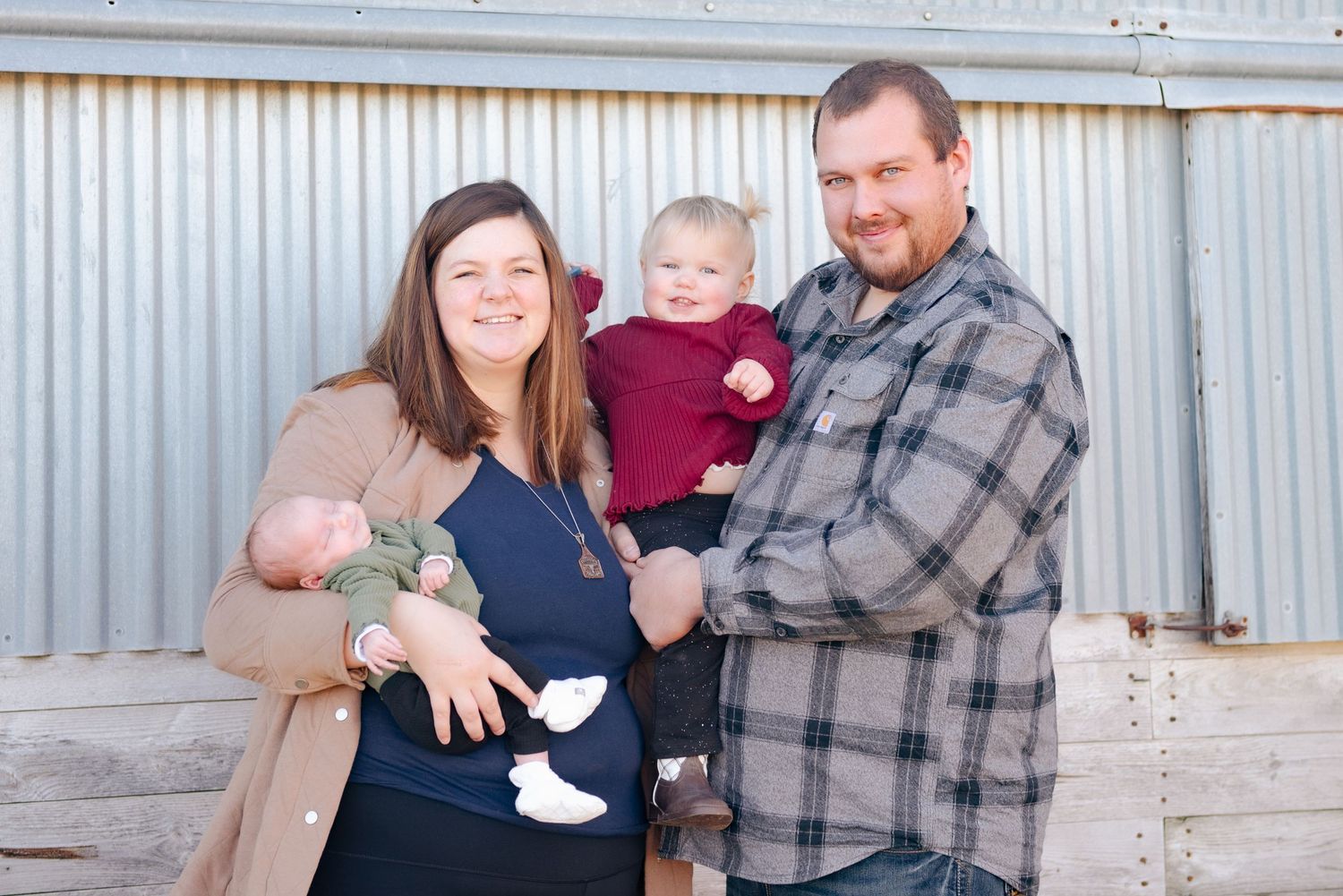 Family of three poses together against a metal wall outdoors.