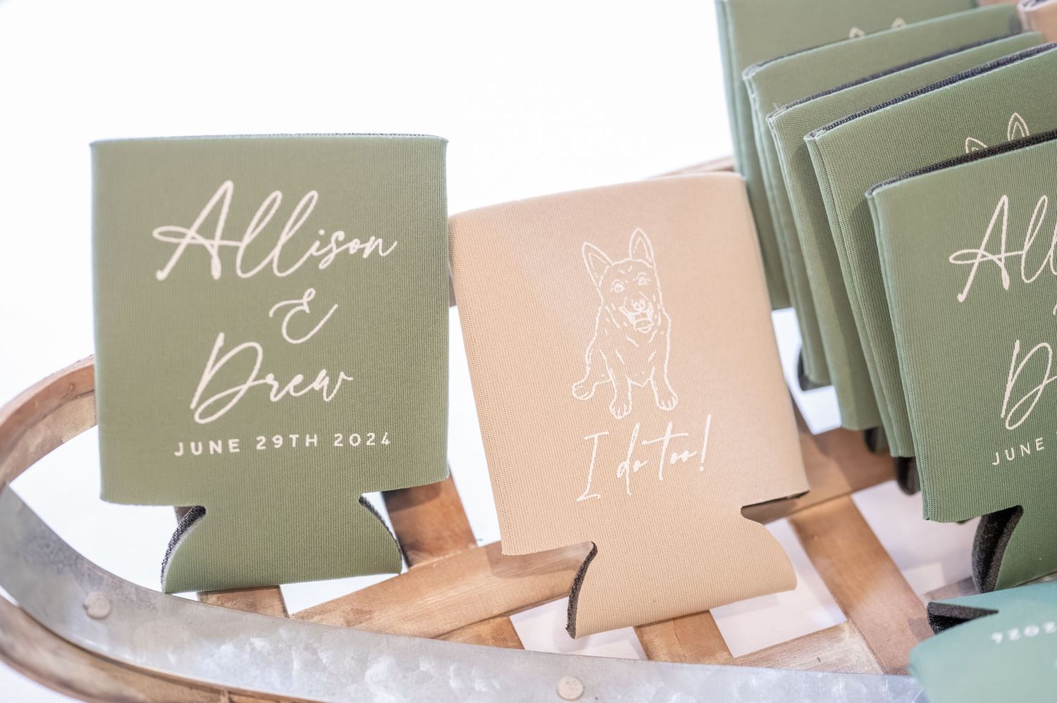 Custom wedding koozies displayed on a decorative tray with sage green and blush pink colors.