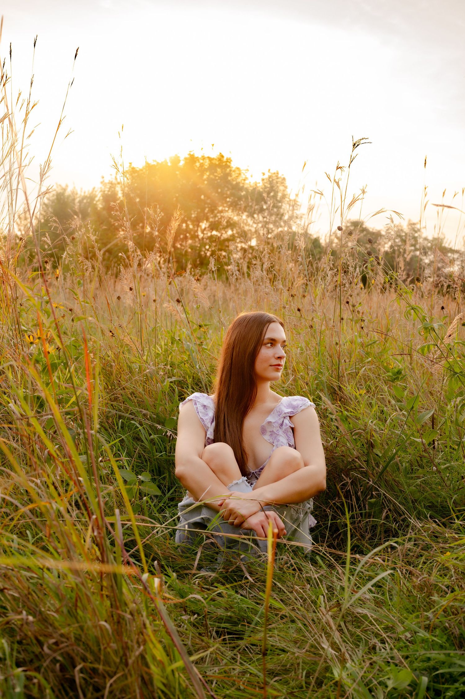 A person sits peacefully in a sunlit meadow of tall grass and wildflowers during golden hour.
