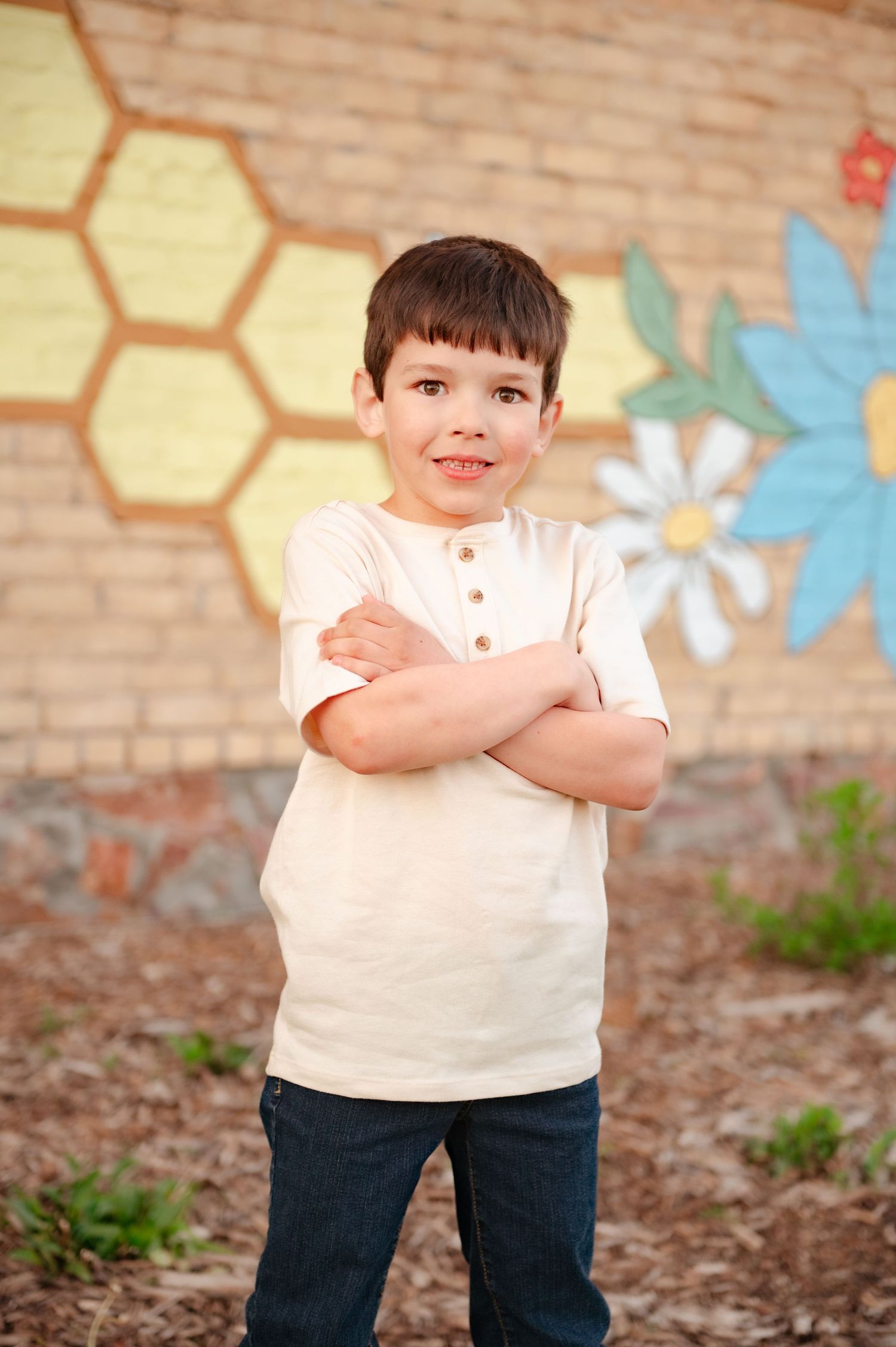 Confident pose in white henley shirt against brick wall with painted flowers and honeycomb design.