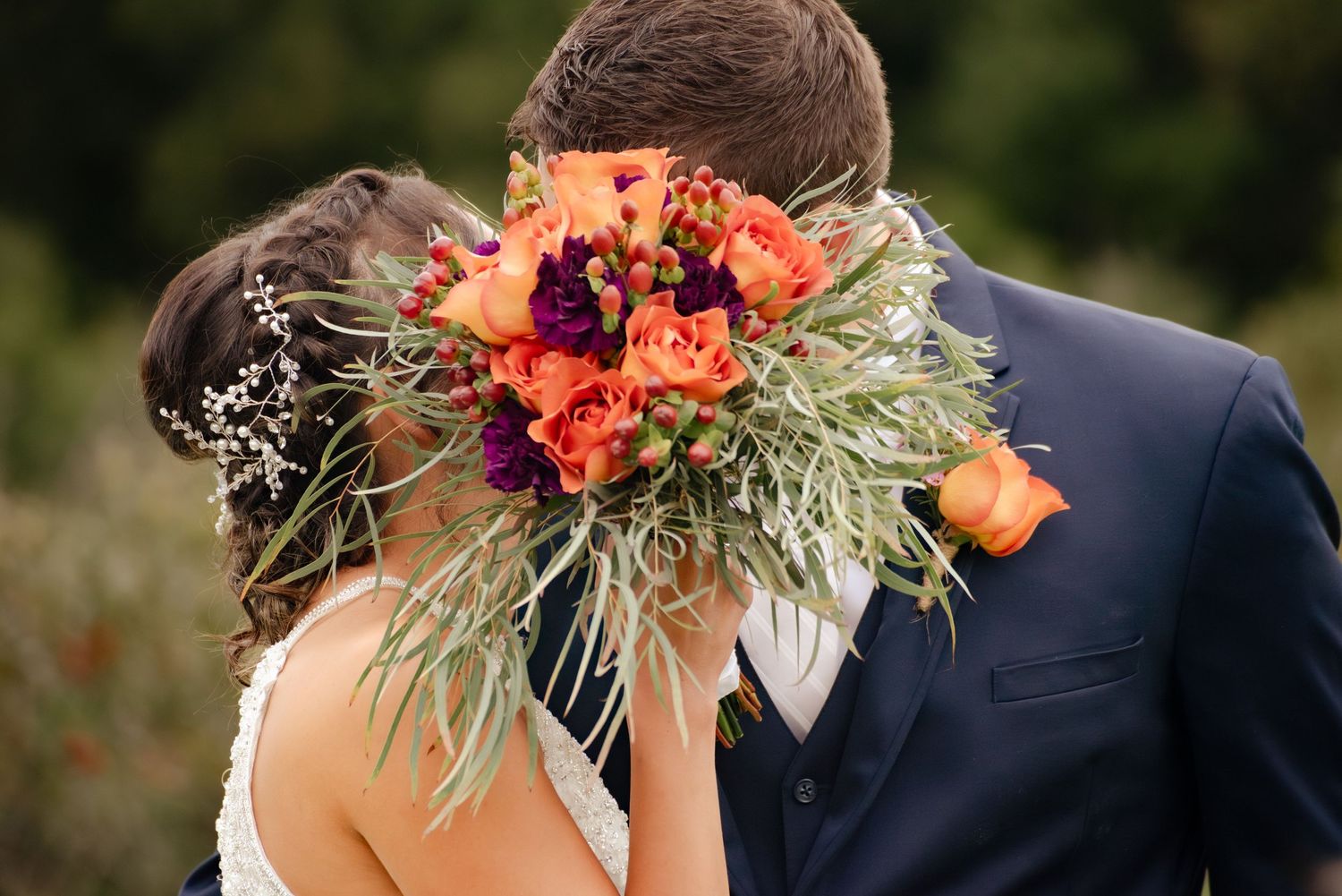 A closeup of a bridal bouquet with coral flowers and greenery during an intimate moment.