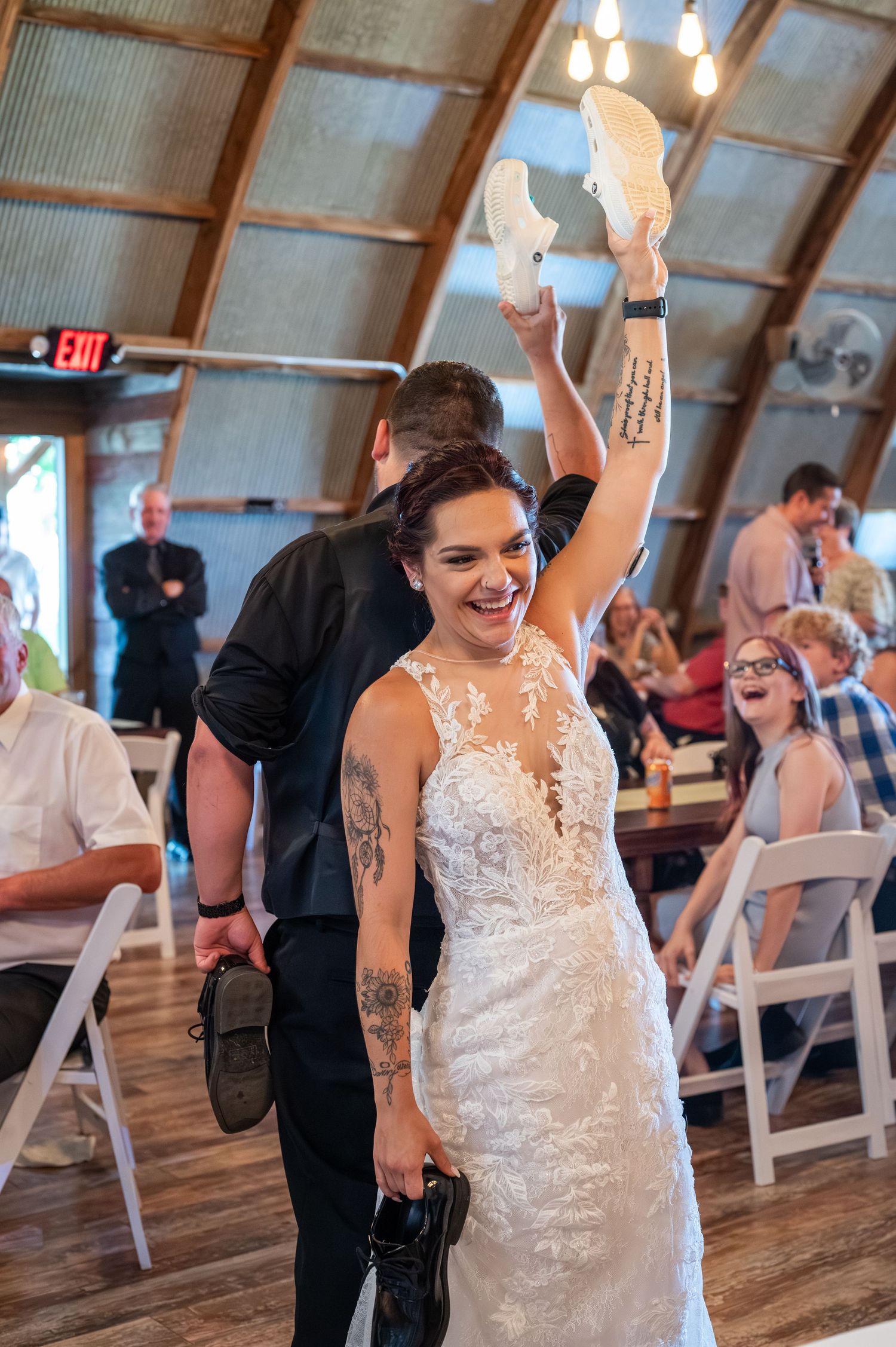 Bride in lace dress celebrates joyfully on the dance floor while holding boots up in the air.