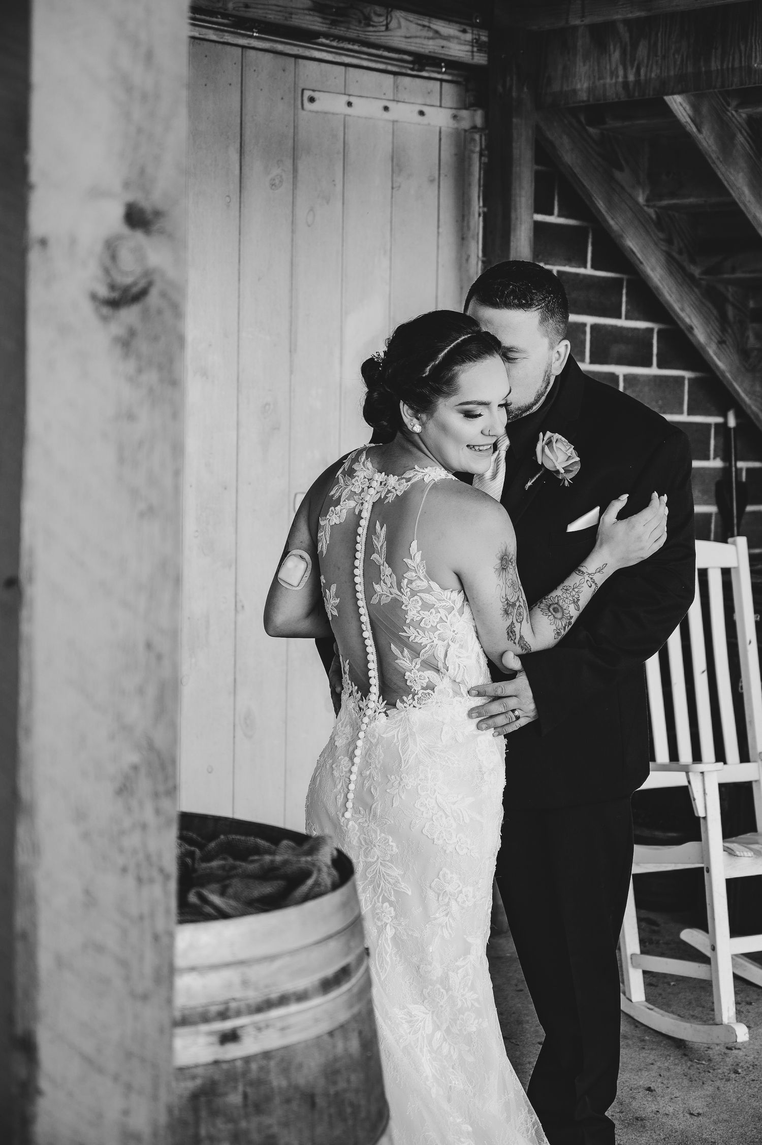 Black and white photo of couple sharing intimate moment during wedding by rustic barn setting.